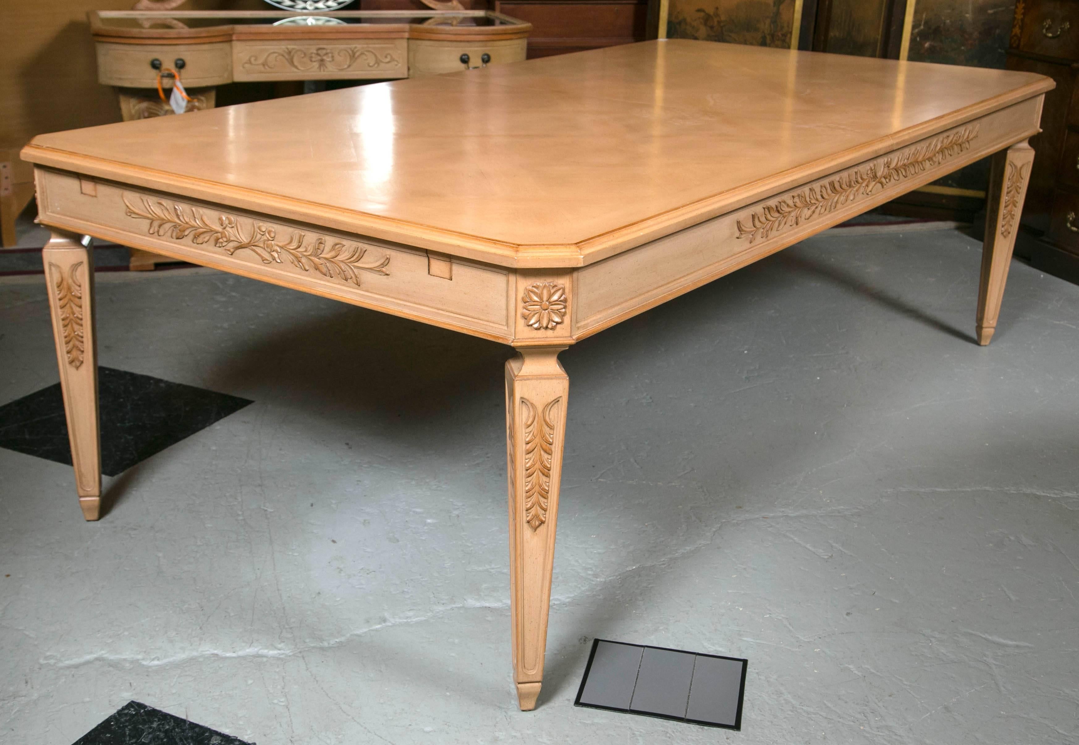 A Grosfeld House Furniture Company Monumental Louis XVI style solid blonde wooden dining table. Displaying Acanthus Leaves along the sides and top of the legs. A beautiful medallion is on all four corners giving this subtle piece the grandeur it