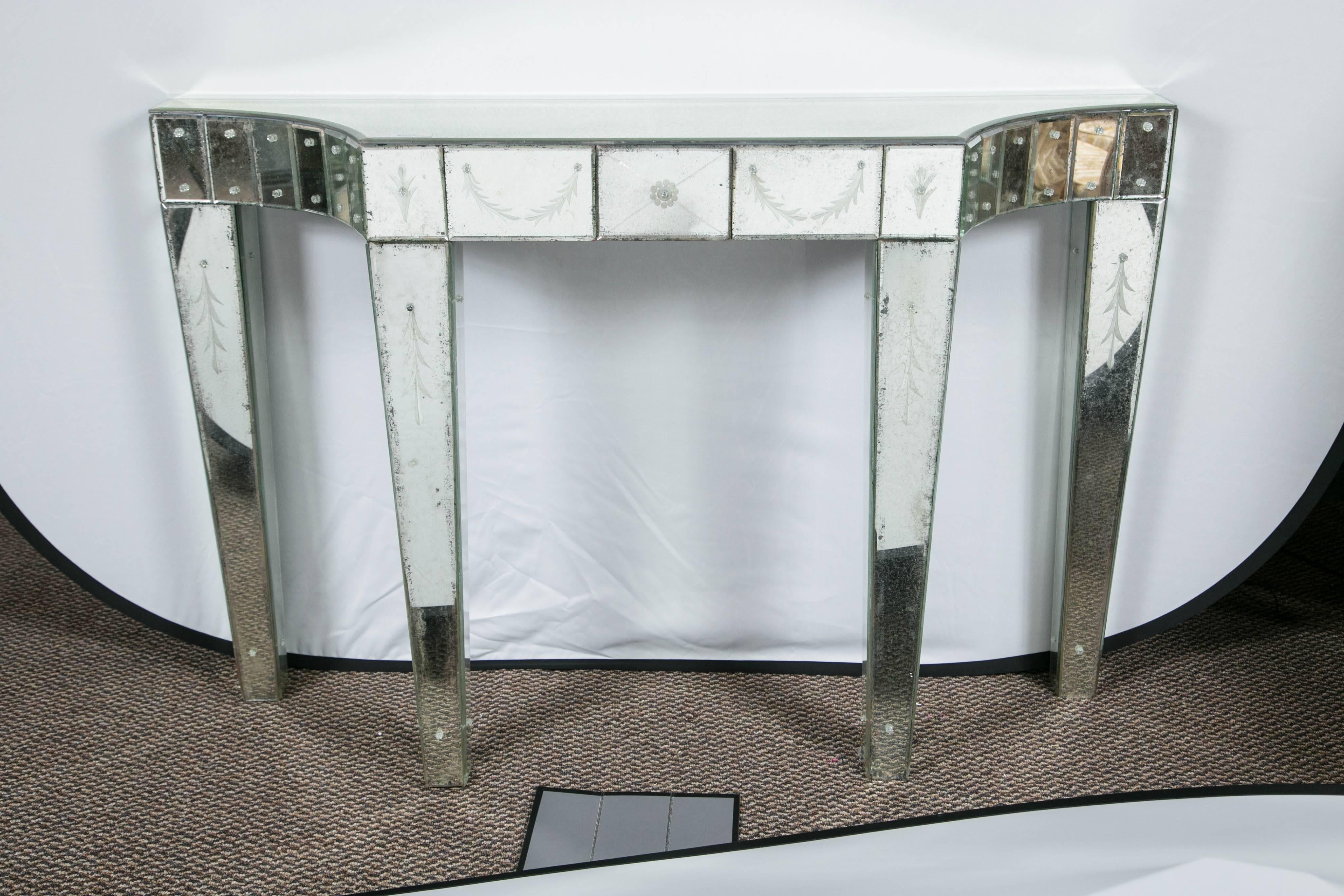 Fine pair of custom quality etched mirrored Hollywood Regency console tables. A combination of traditional and Mid-Century Modern is used in this exquisite piece. Etched leaves on the front of the legs top corners and the side of the front apron has