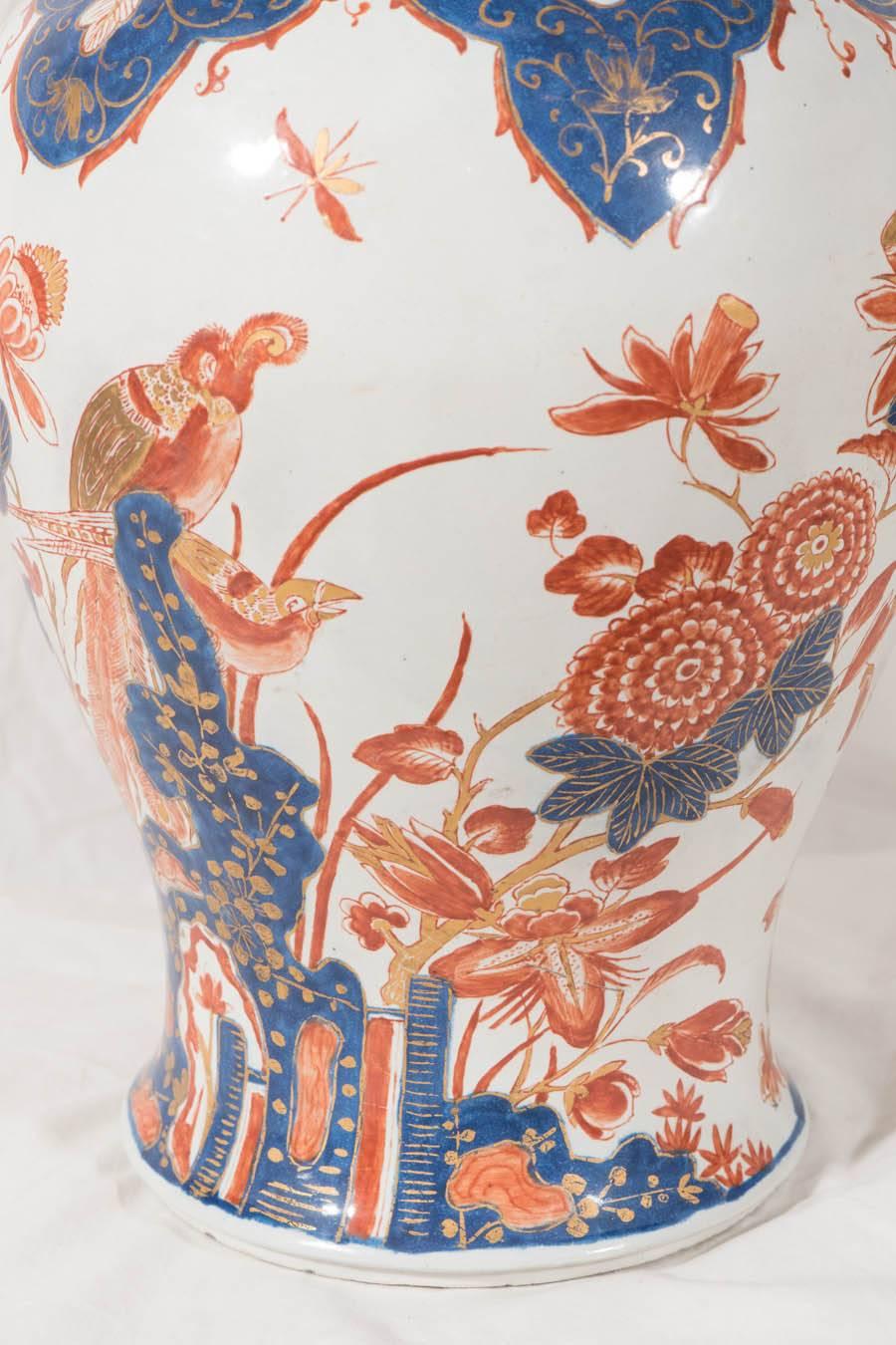 A pair of Dutch Delft covered jars decorated in the Imari style of Delft Doree. Each vase is hand-painted in deep cobalt blue and red with gold gilding. The decoration shows a garden scene of long-tailed birds amid chrysanthemums and peonies.
 