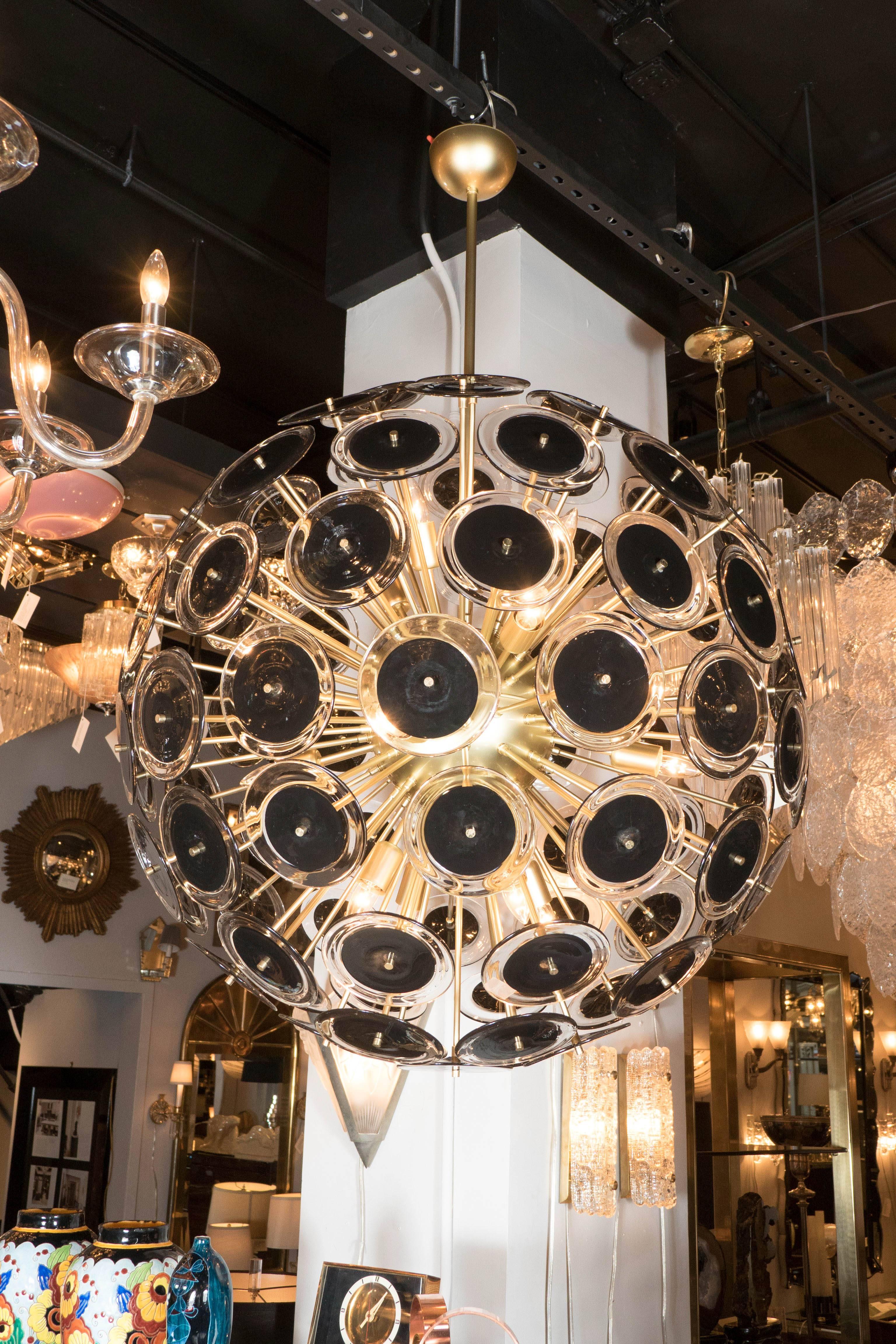This outstanding modernist Sputnik chandelier style of Vistosi, features a satin finished brass frame with a spherical core from which numerous rods emanate. At the end of each rod is a hand blown Murano glass disc with a black center with clear