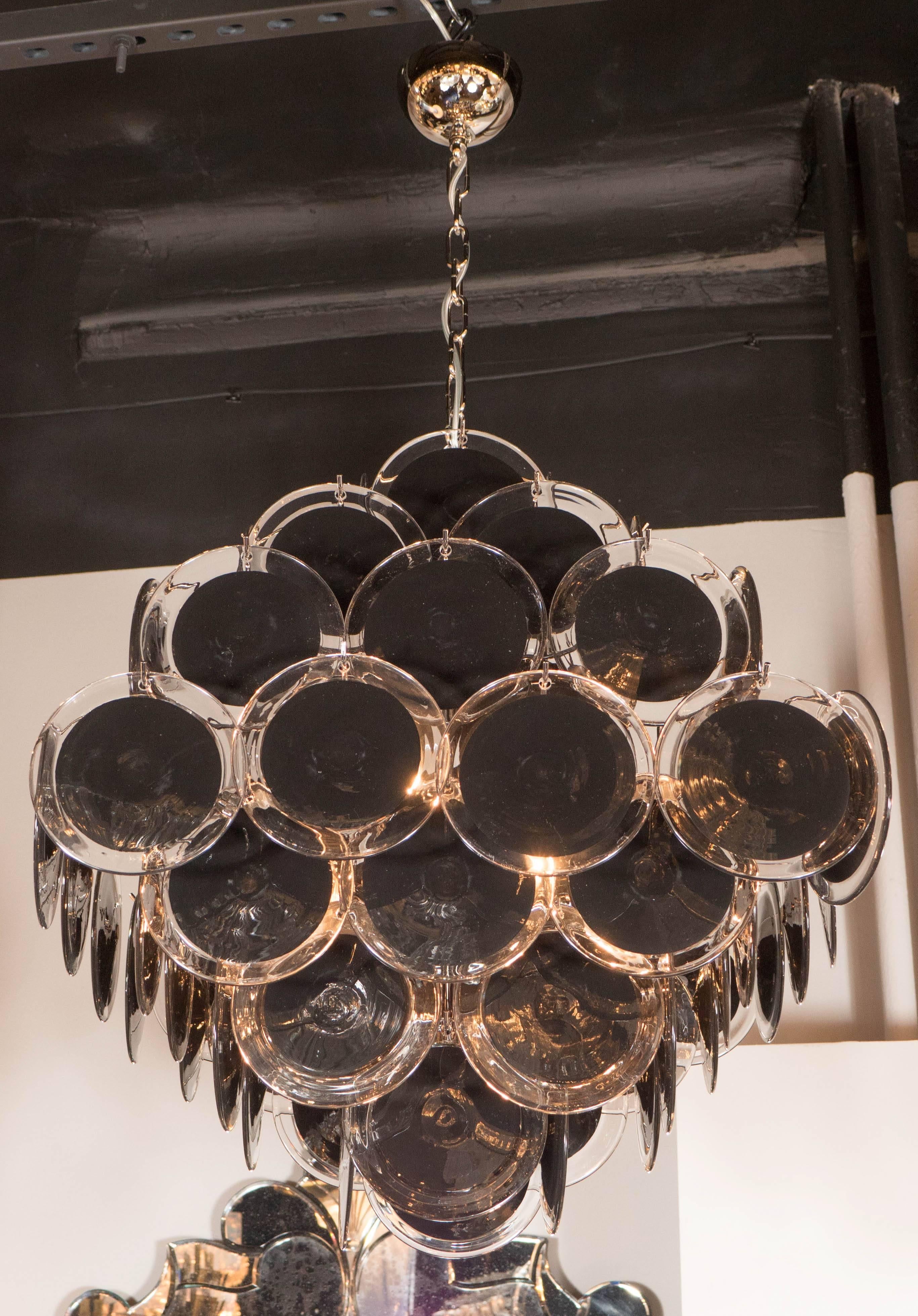 This chic Modernist chandelier by Vistosi displays 64 handblown black and clear Murano glass discs suspended in a diamond formation. Each disc is made by hand and incorporates a black center suspended in the glass. The fittings are polished chrome,