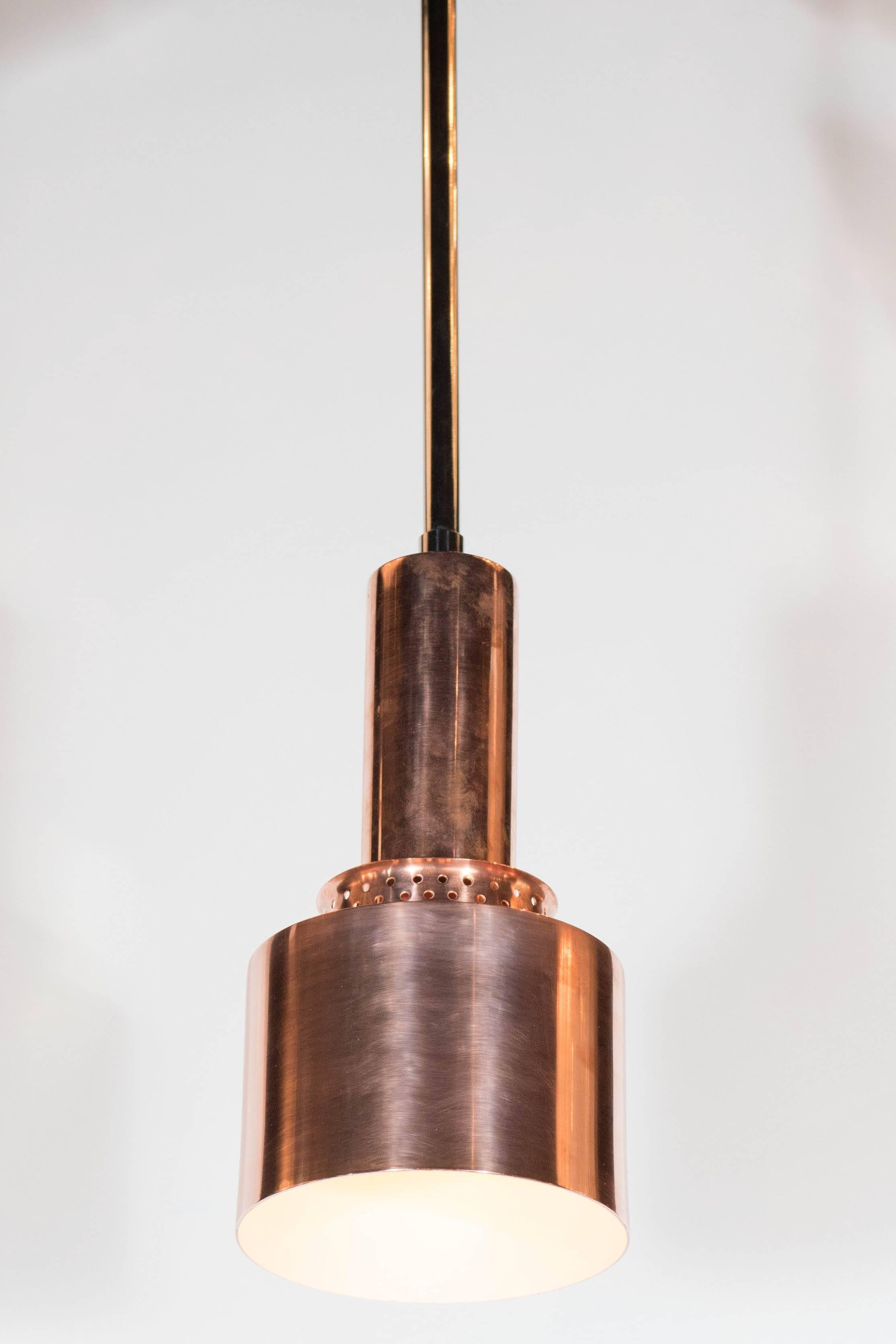 Ciondolo in rame in stile Mid-Century Modernist dal design pulito e industriale. Il rame lucido e la fascia traforata conferiscono un'estetica minimalista. Il paralume e il baldacchino sono in rame lucido, mentre il braccio del ciondolo è in cromo