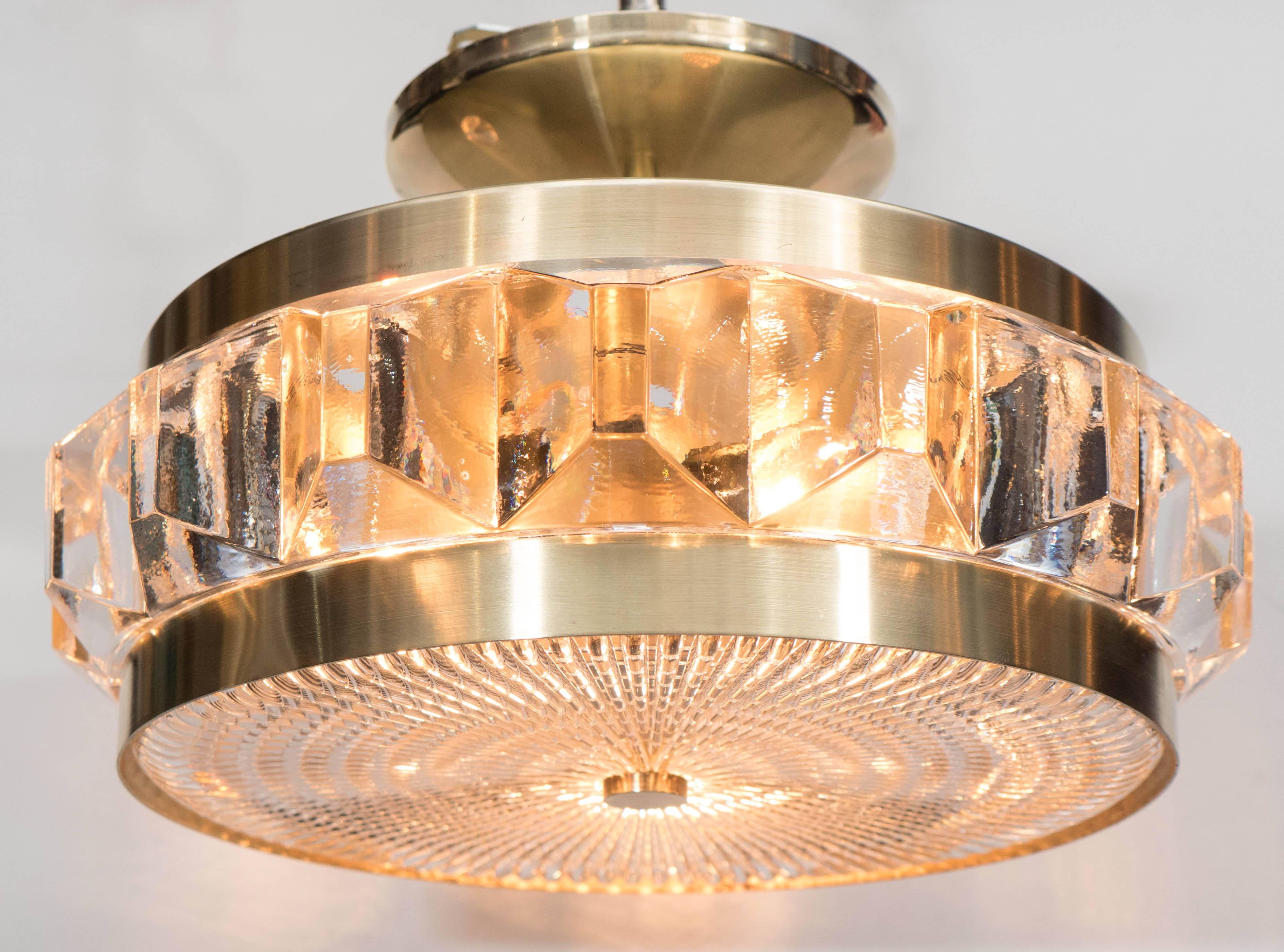 Gorgeous Mid-Century Modernist flush mount pendant chandelier with textured glass and brushed brass fittings by Orrefors. Parallel brass bands encase a textured glass disk supported by a brass fitting, as well as a faceted glass band. A very elegant
