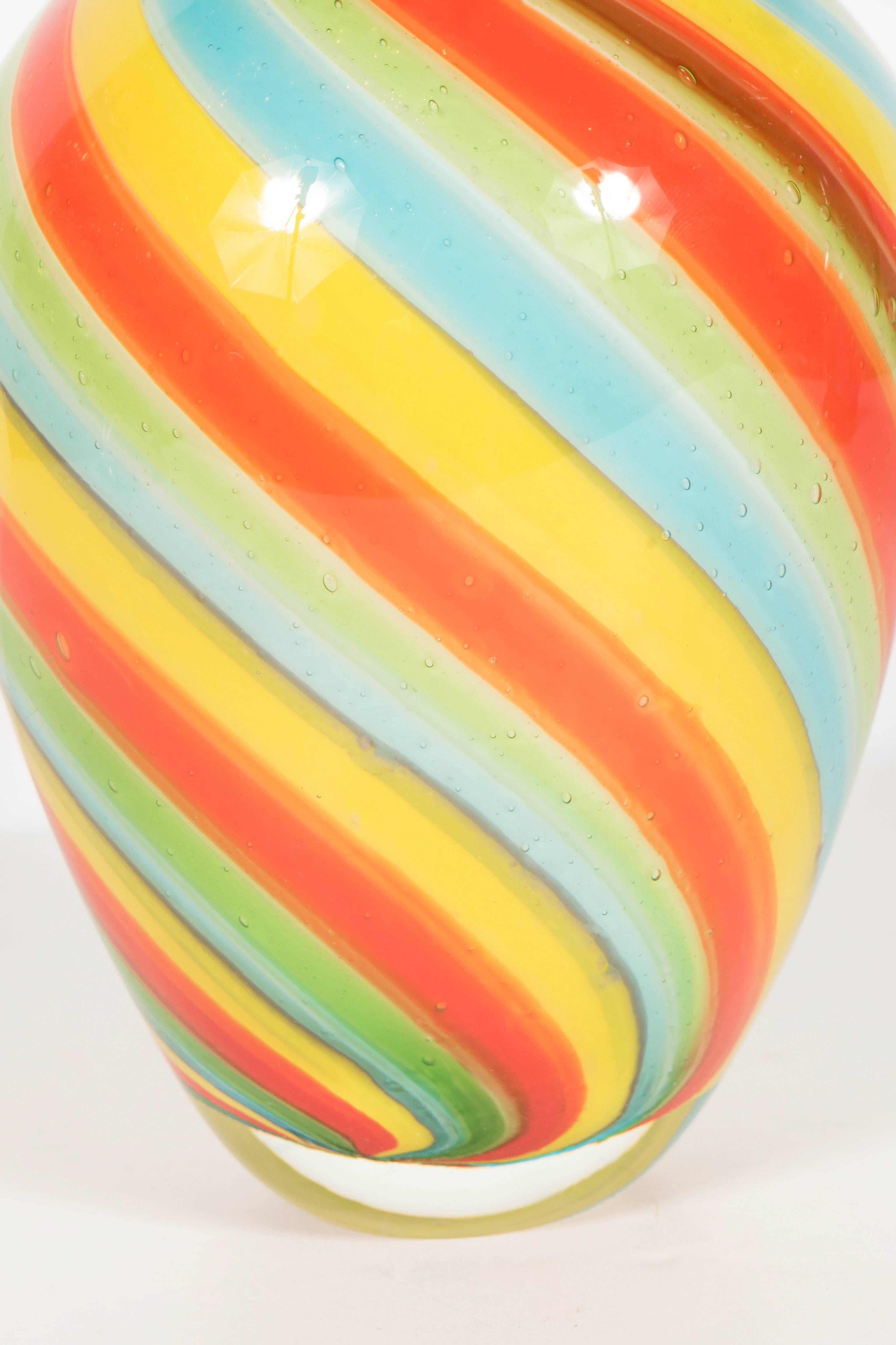 A radiant Murano vase with hand blown and multi-colored candy striped glass.  Campari orange, Chartreuse green, sky blue and yellow candy stripes form a swirling pattern along the piece. This would make a colorful and dynamic addition to any room,