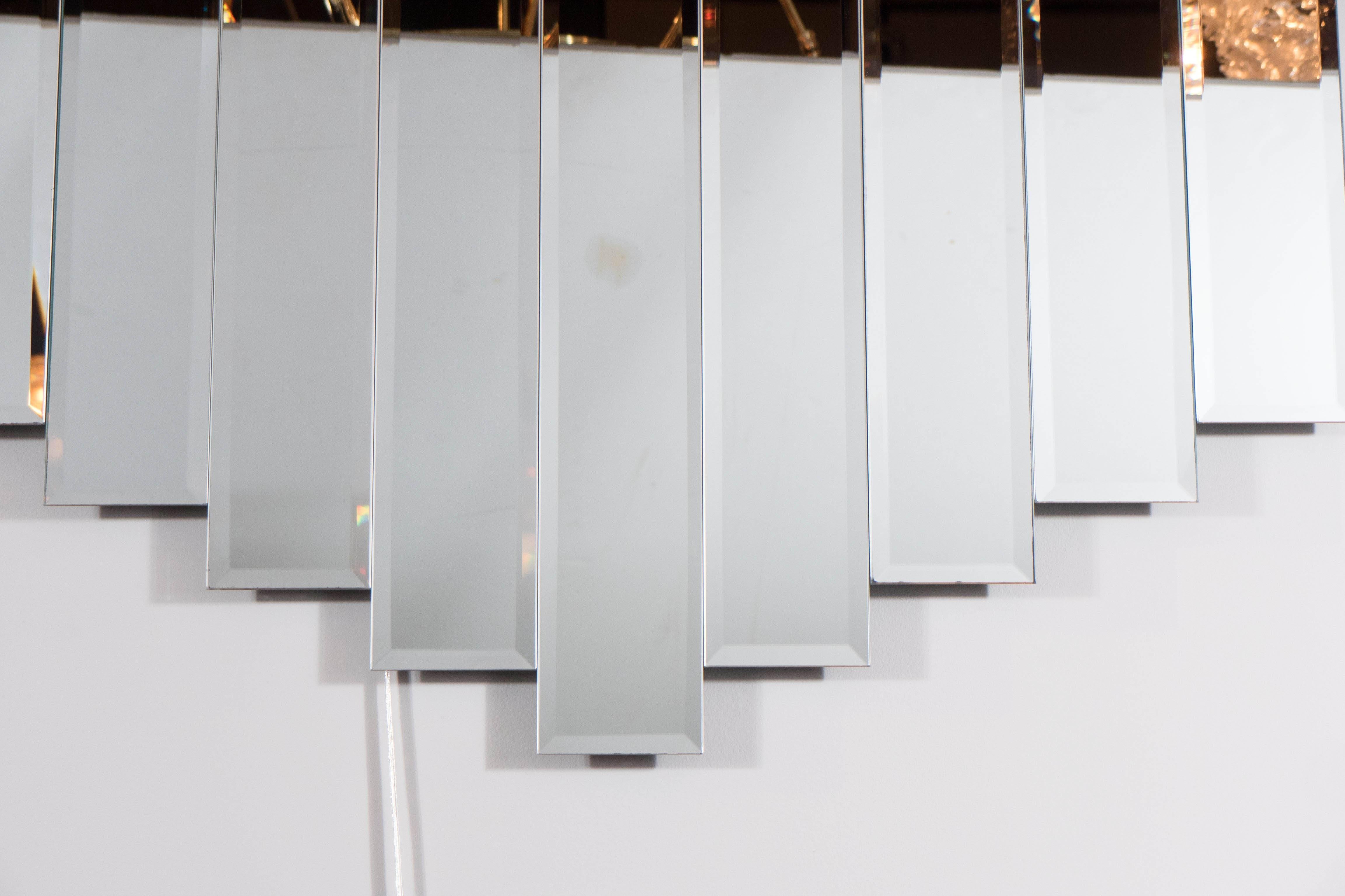 This sculptural Mid-Century Modernist wall mirror consists of nine long mirrored panels in a symmetrical geometric formation. Each panel is hand bevelled and this mirror is in excellent condition. This piece is also sculptural wall art as well as
