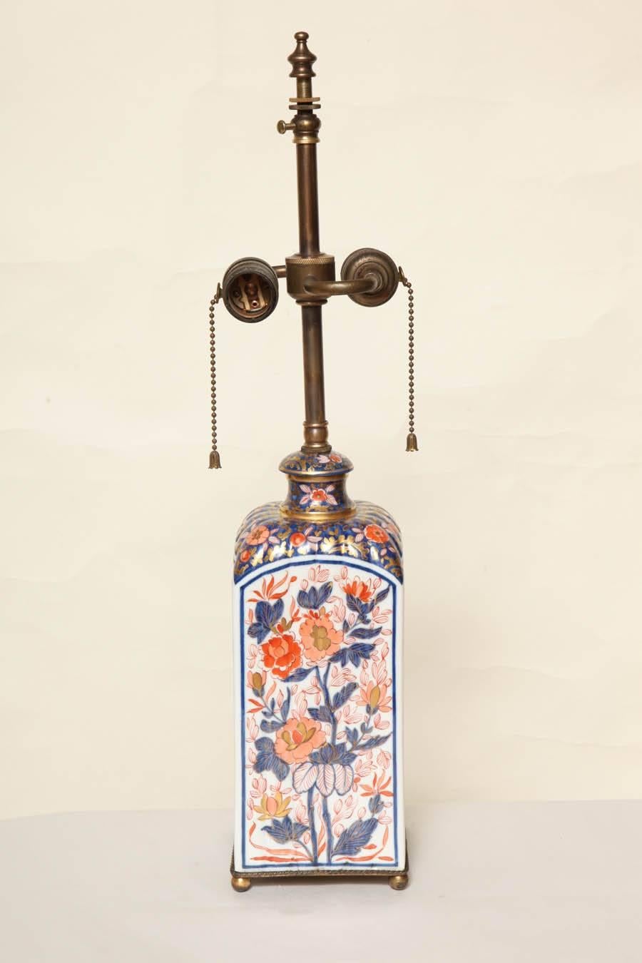 A pair of Japanese Imari square sided sake/wine bottles and covers, now mounted as a pair of two-light table lamps, early 19th century. Featuring a ribbed surface and each panel decorated with flowering trees in the Imari red and cobalt blue