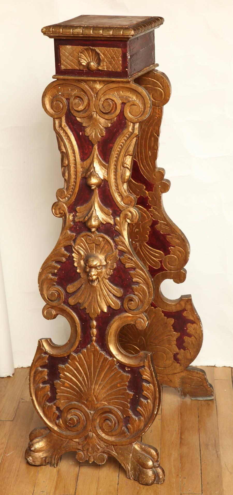 Italian Baroque style carved wood pedestal of an X-shaped easel form on massive lion paw feet, circa 1940. Featuring a painted Pompeii red ground and decorated with carved and gilded S and C-scrolls, satyr heads, shells, fruit and flowers. Top