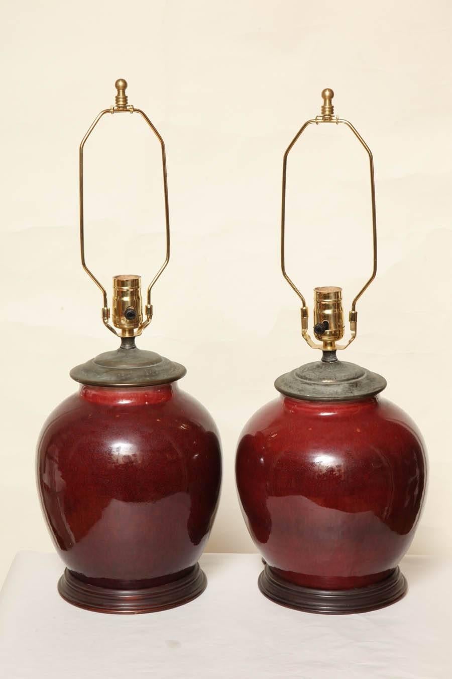 Pair of Chinese globular shape porcelain vases, oxblood glaze, mounted as single-light table lamps. Turned wooden bases and metal vase camps. Vase Height 10 Inches.
