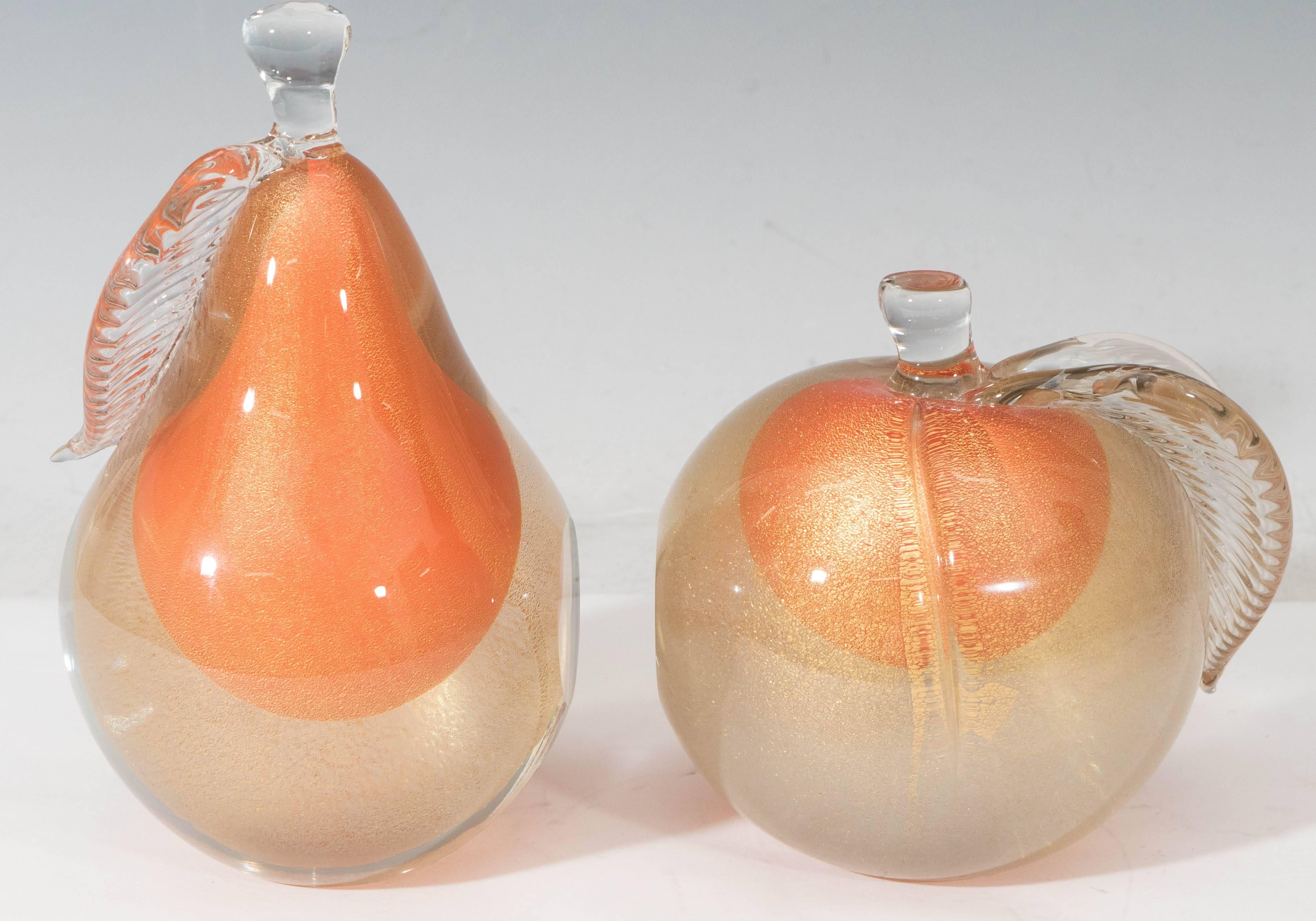 These Italian art glass pear and apple bookends by Alfredo Barbini, produced circa 1950s to 1960s, each come in clear sommerso layer with flecks of gold, over a bright orange toned center; both bodies have a flat polished end, to support books set