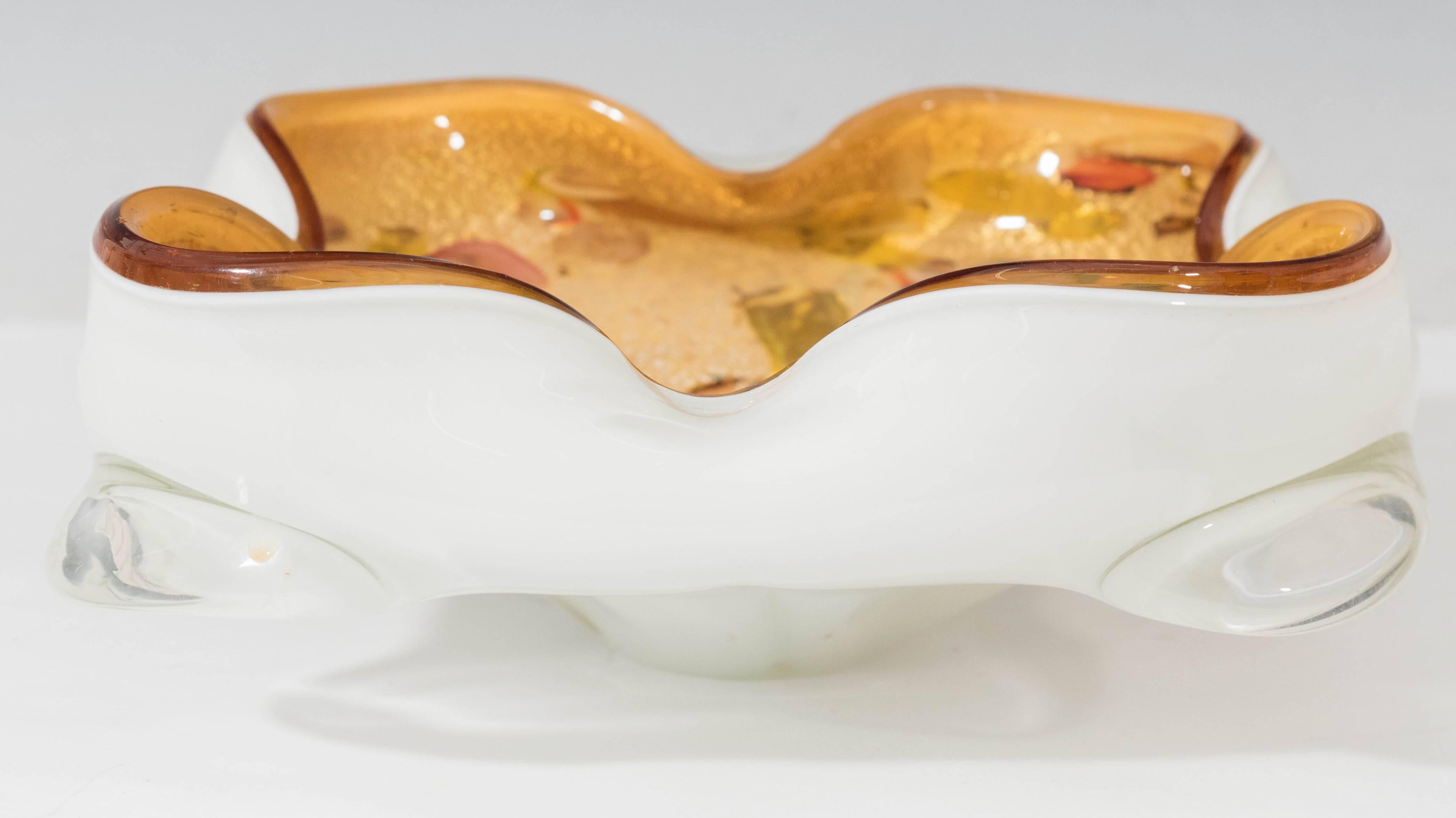 Vintage Murano art glass bowl, with four round folds to the scalloped rim, the exterior white and encased in clear glass (rendered with Sommerso technique), the interior amber toned, decorated with multicolored splashes and aventurine flecks. This