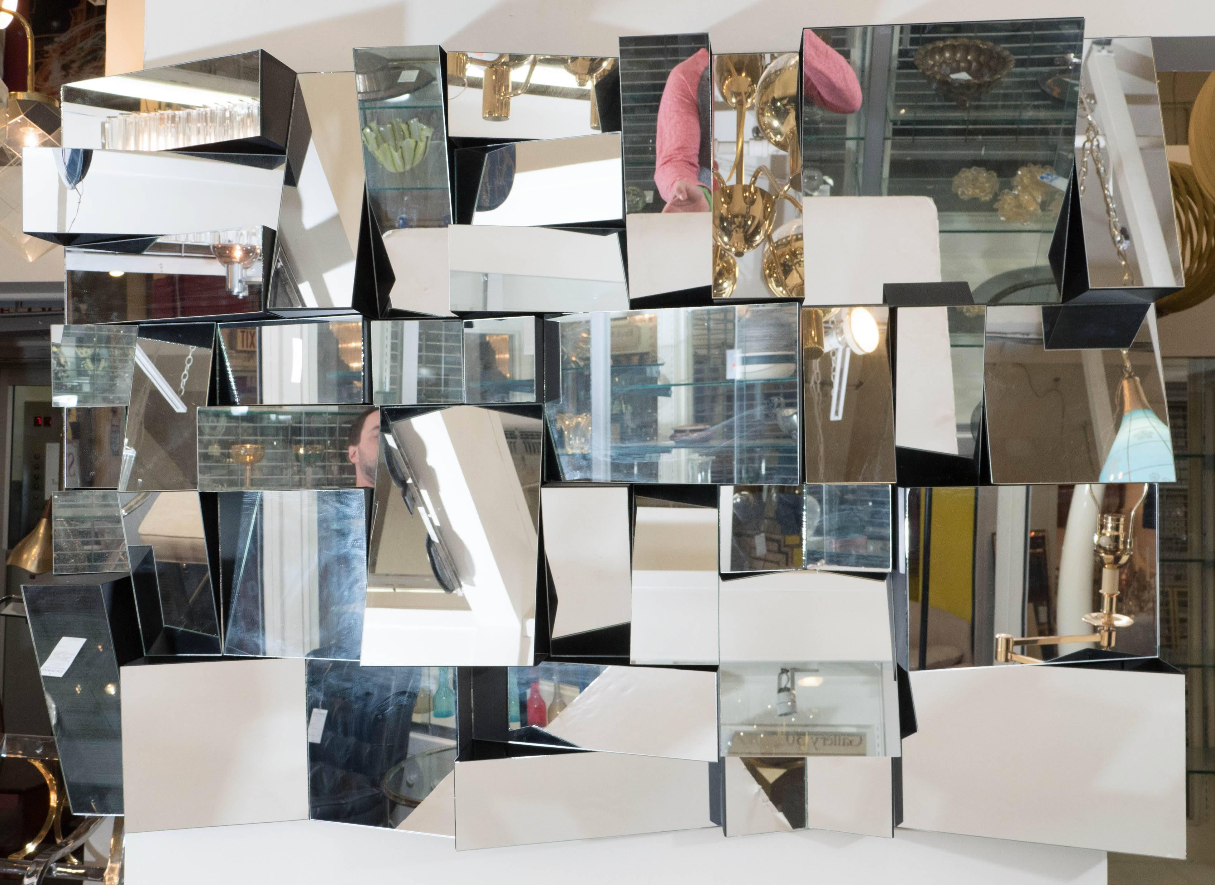 A large-scale wall mirror, following the manner of the 'Slopes' design by Neal Small, composed of assorted square and rectangular mirrored panels, each projecting from the wall at a varied angle, which creates a highly modernist, fractal appearance;