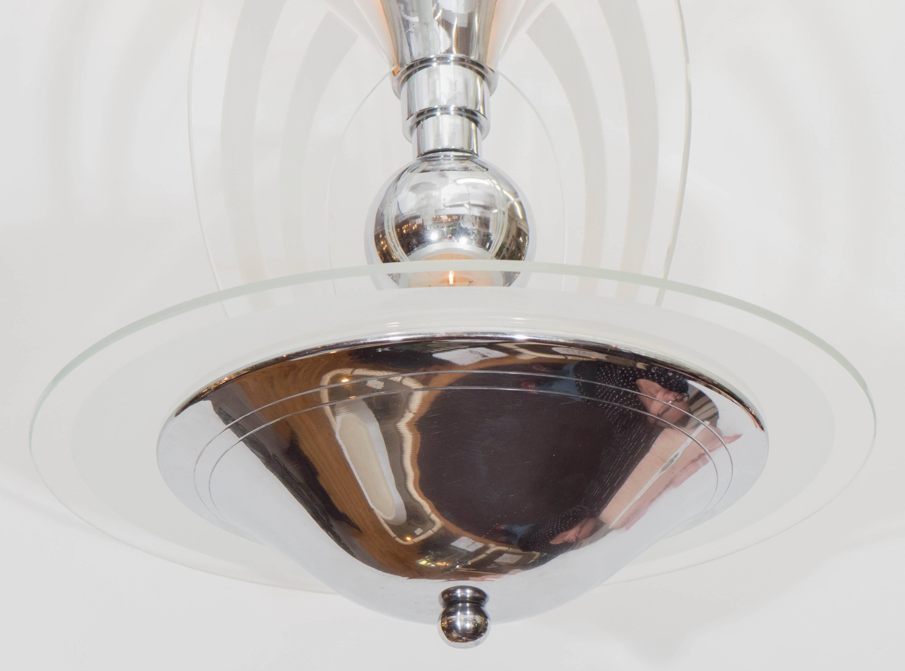 This Art Deco chandelier in polished chrome, produced in France, circa 1930s, includes artfully formed dual shades, one a rounded convex, the other an inverted tapered cone, with central ball, decorated with curved glass panels, etched with frosted