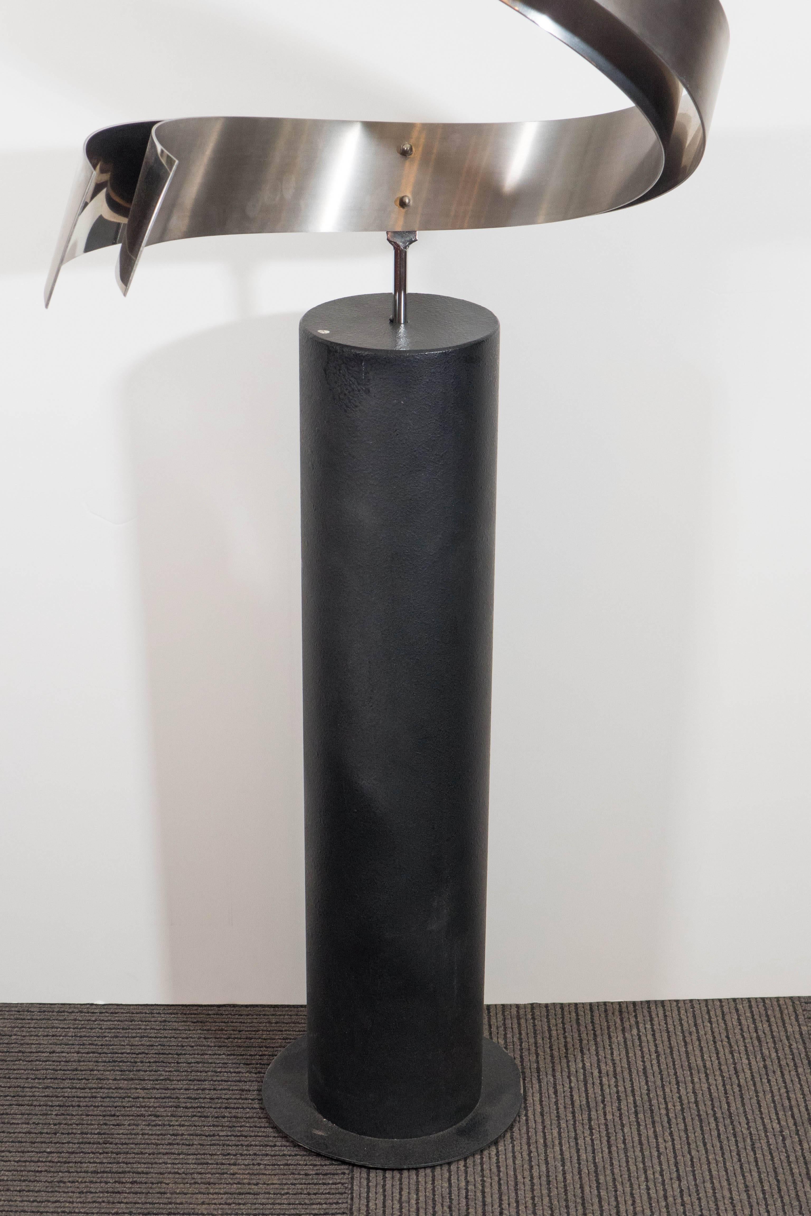 A contemporary modern abstract sculpture, produced by Curtis Jere, circa 1990s, composed of dual sheets of steel, worked into swirling 'ribbon' shapes, brushed and polished on opposite sides, raised on a lengthy, cylindrical black iron floor stand.