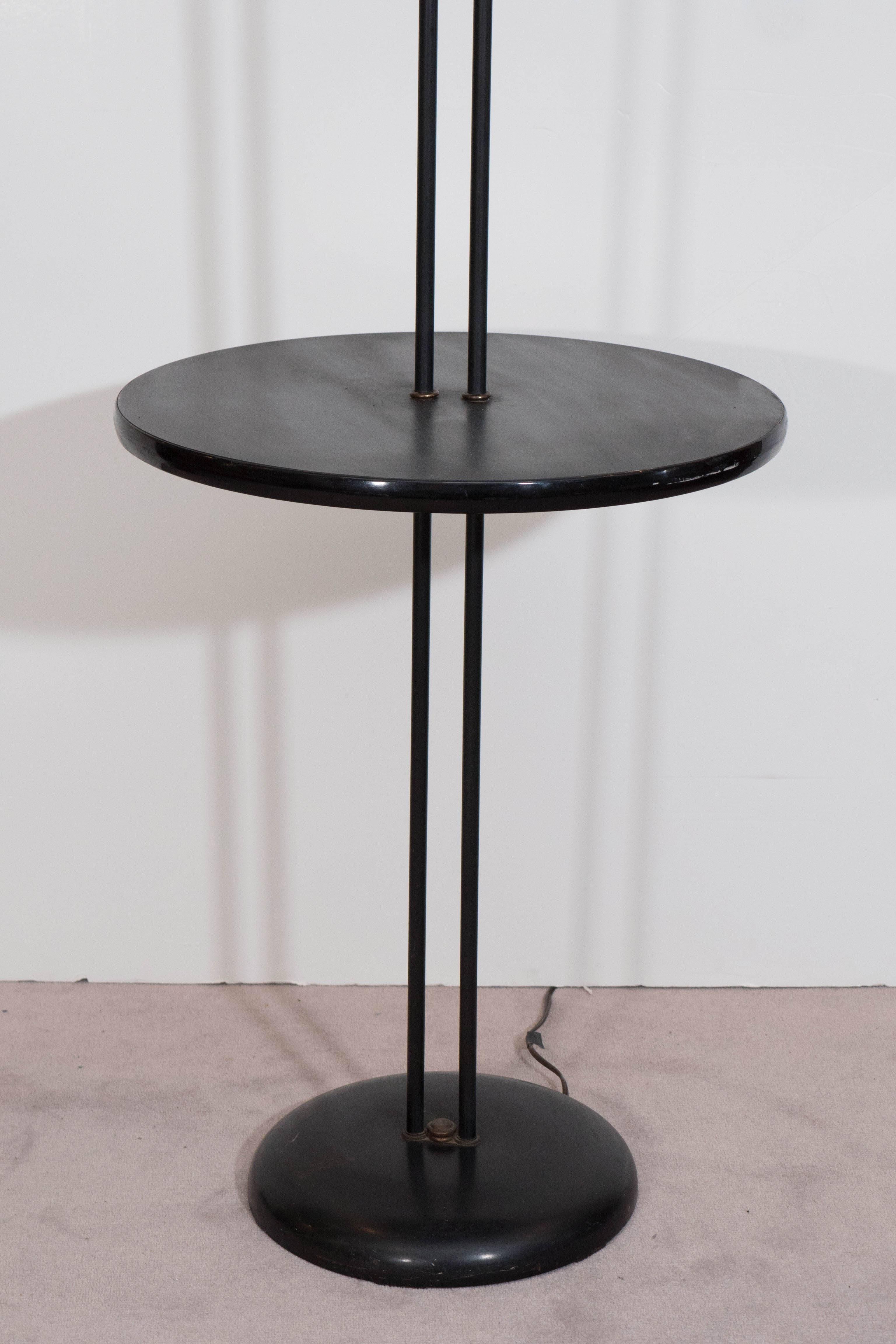 A floor lamp with two lights, each with single socket and cone form fiberglass shade, supported by adjustable gooseneck, on lengthy black enamel stems, joined by a round table in laminated wood. Despite presence of wear, including age appropriate
