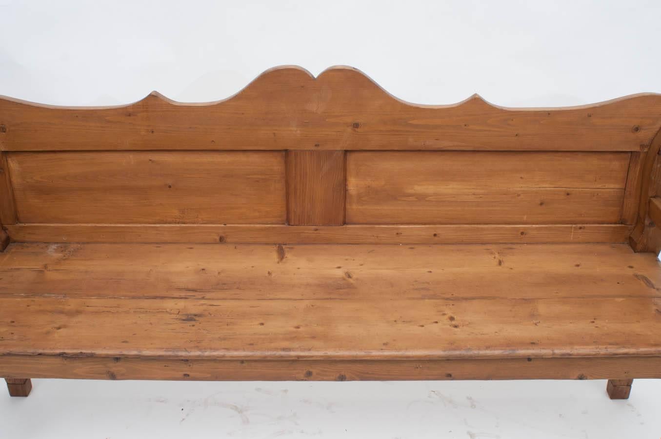 A beautiful pine bench or settle with a boldly scalloped back rail above two flat panels.  The scrolled arms are contiguous with shapely cabriole legs.  The deep two board seat is supported on all four sides by a straight morticed-in apron with two