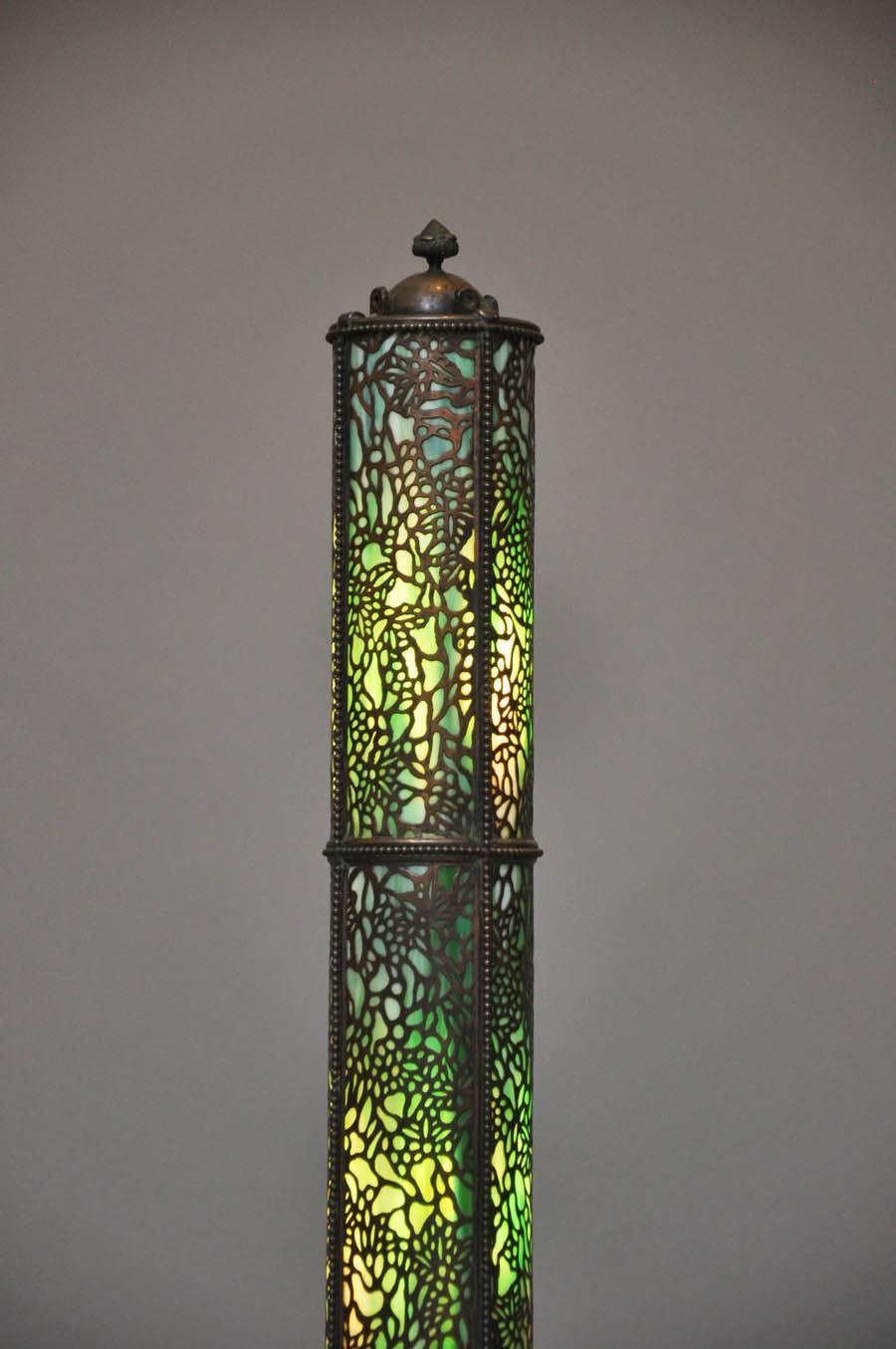 This rare and large Art Nouveau Tiffany inspired mosaic design with green glass, copper and bronze floor lamp with tubular shaped stained glass body overlaid with copper filigree and bronze beading border, a copper crown with acorn finial, lamp