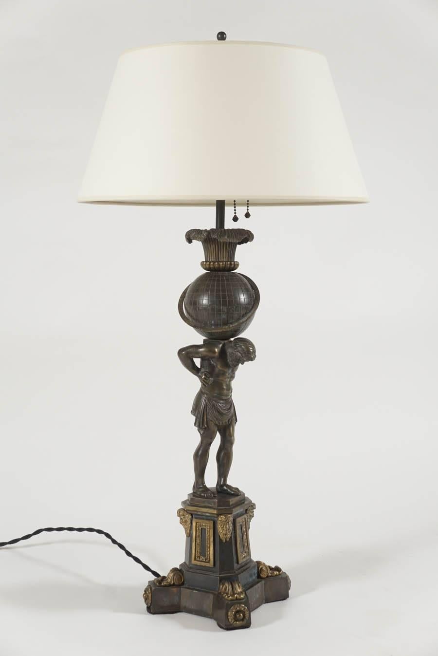 English William IV period, bronze table lamp by the Birmingham firm of Thomas Messenger and Sons depicting Atlas supporting the earth with swiveling ring on quadraform plinth base with panel, god-head, and acanthus motifs.  Originally a sinumbra