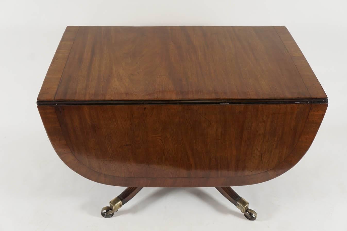 Fine English, George III period, circa 1800 mahogany drop-leaf breakfast table having cross-banded reeded-edge top on ring-turned tapered pedestal issuing four reeded down-swept splayed supports terminating in original brass caps with dramatic