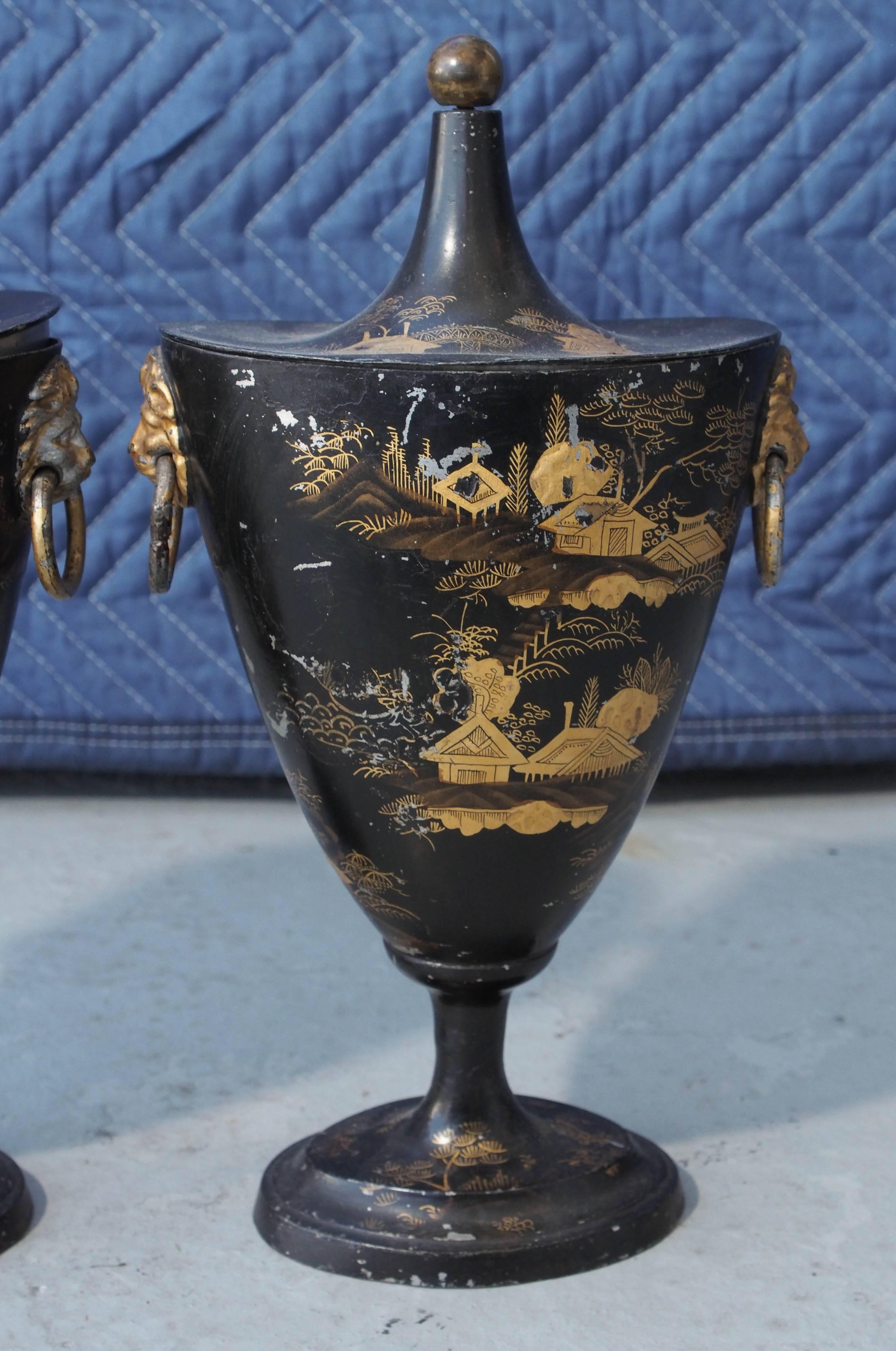 Pair of early 19th century tole chestnut urns with chinoiserie decoration with conical lids in ovoid form. Ringed gilt lions head handles and ball finials.
