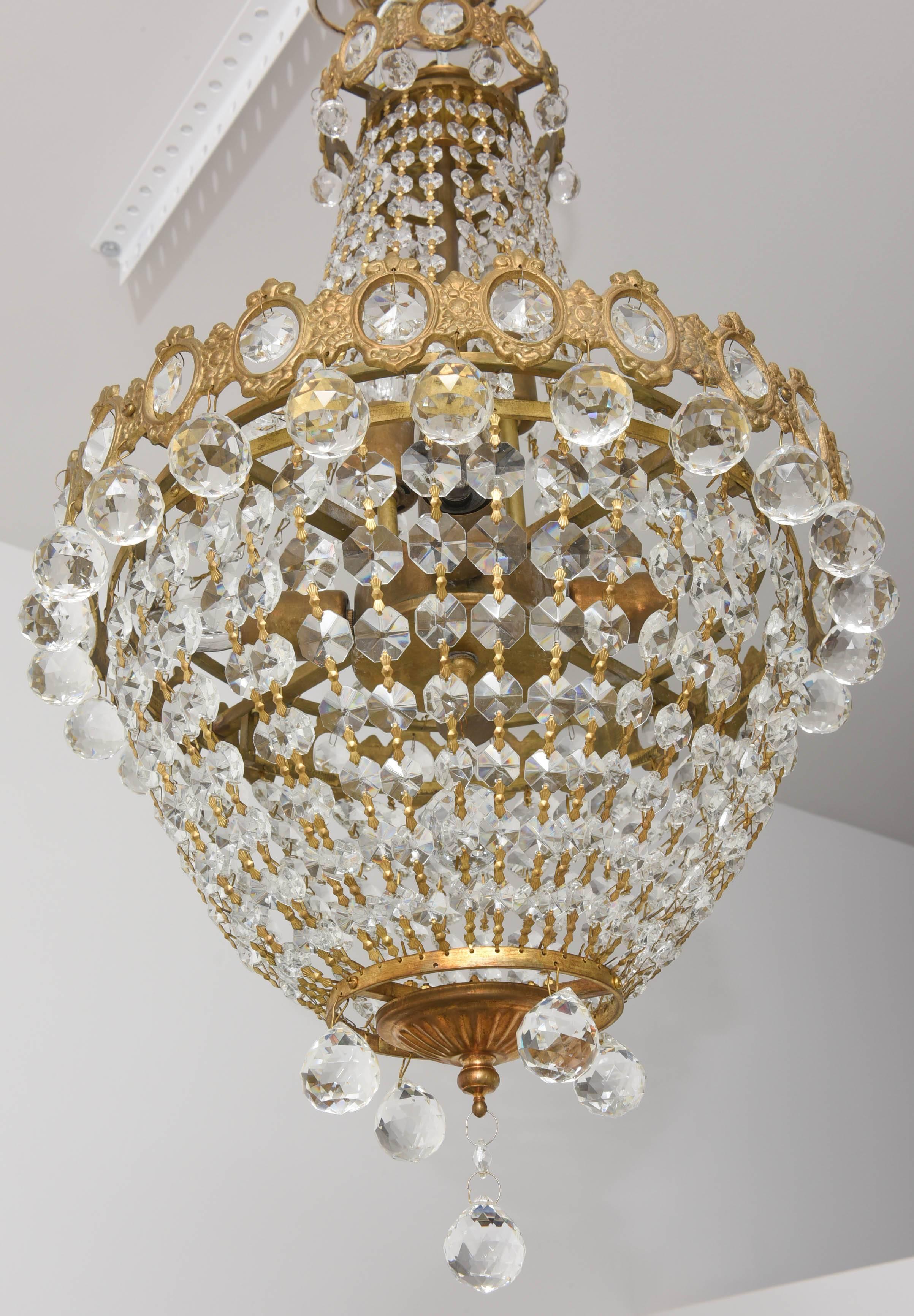 This beautiful Hollywood Regency style chandelier takes its inspiration from the court of Louis XVI. The brass has mellowed to an antique color which works beautifully with the faceted crystals. 

Note: This piece requires six candelabra based