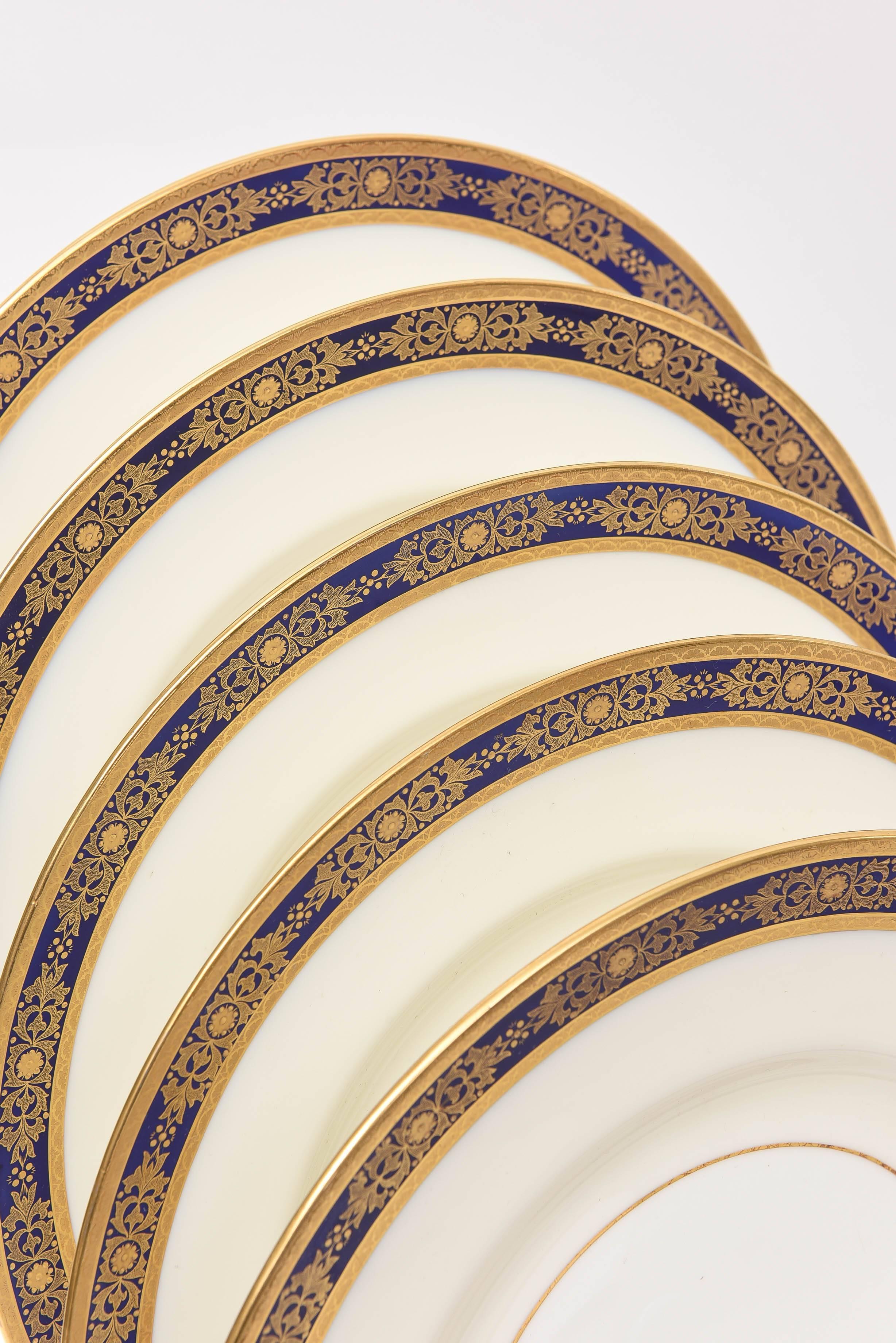 A set of 12 dinner plates by one of our favorite makers, Minton England. Custom ordered and made for Tiffany. These 12 plates feature 2 crisp 24k acid etched gilt bands with a nice design of raised tooled gold in a cobalt blue band on its collar. An