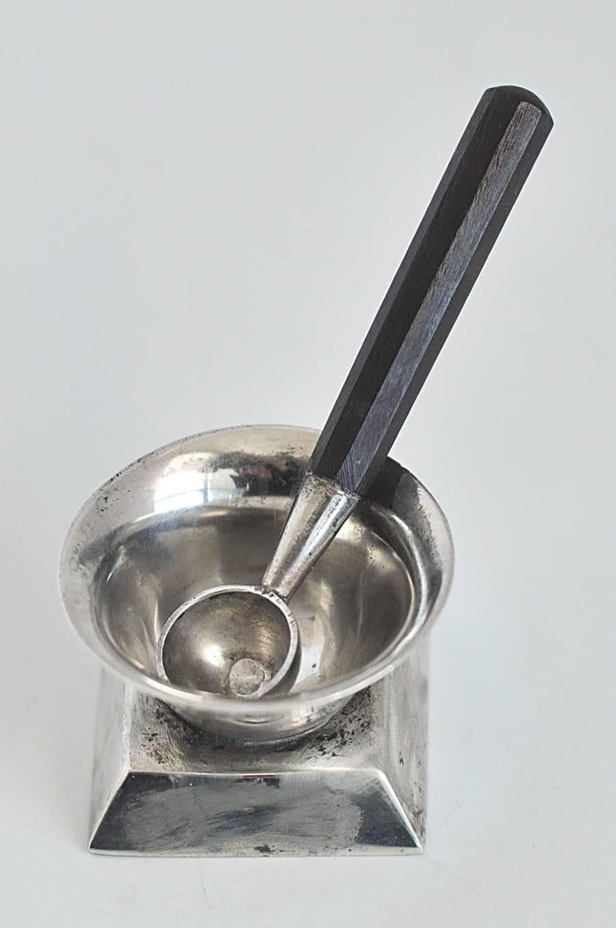 A modern sterling silver salt cellar by the master silversmith William Spratling (1900-1967) from the Art Deco period (1931-1945). Included is a matching spoon with a faceted rosewood handle. Interesting, geometric platform base in the Art Deco