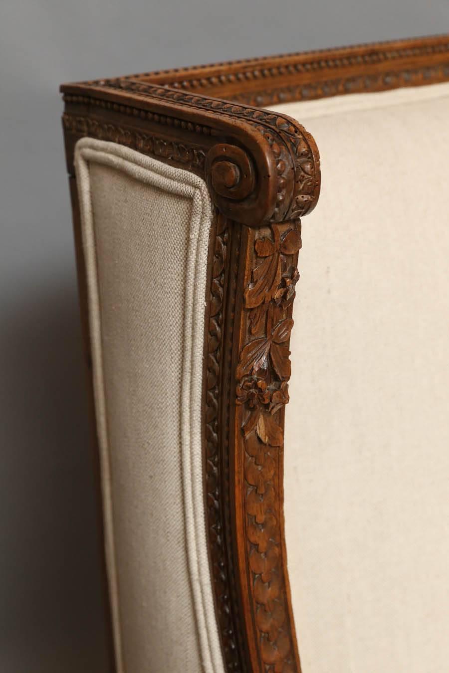 Beautiful Louis XVI style wing chairs with desirable soft aged patina. Newly upholstered in 100% linen with self welt and new padding. Highly detailed carved wood features several motifs such as egg and dart, acanthus leaves, flowers and vines,
