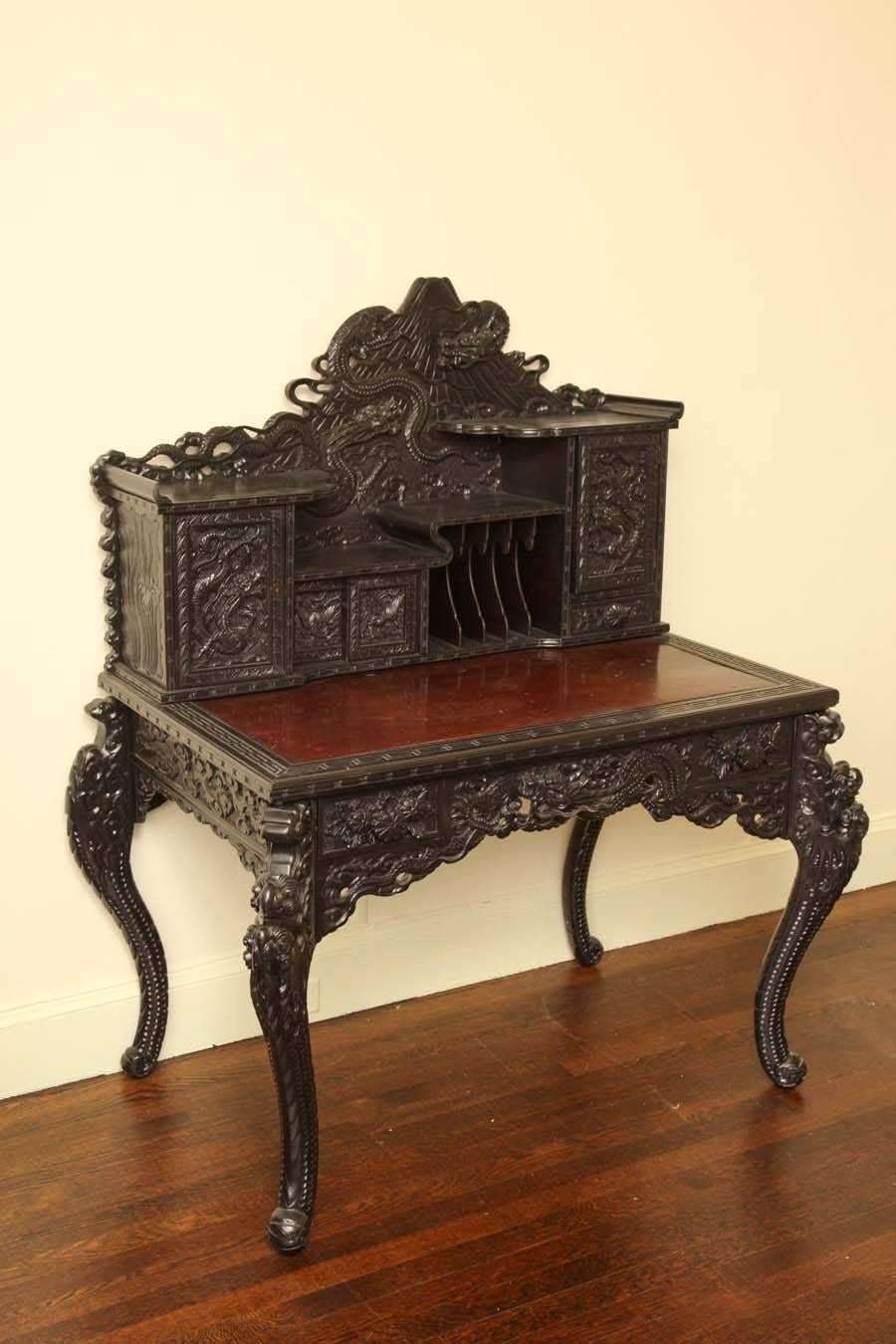 Intricately carved with dragons. The rectangular top surmounted by an asymmetrical superstructure incorporating pigeon holes and drawers, the frieze fitted with two short drawers raised on cabriole legs.