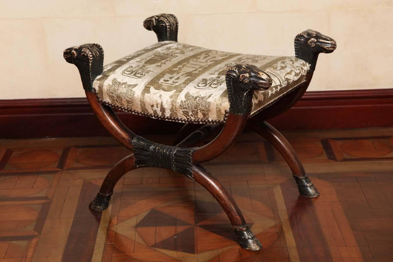 The velvet-upholstered seat on an X-form support with four sheep heads and joined by a turned baluster stretcher on hoof feet. 

The 