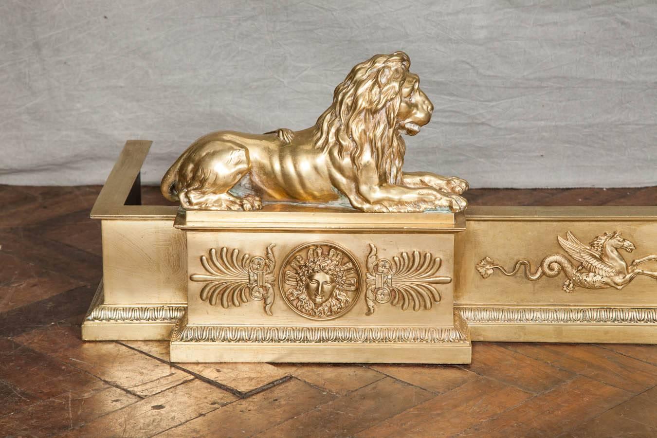 A very impressive large Empire influenced brass fire fender, having a pair of recumbent Lions mounted to either side and classical motifs to the frieze.