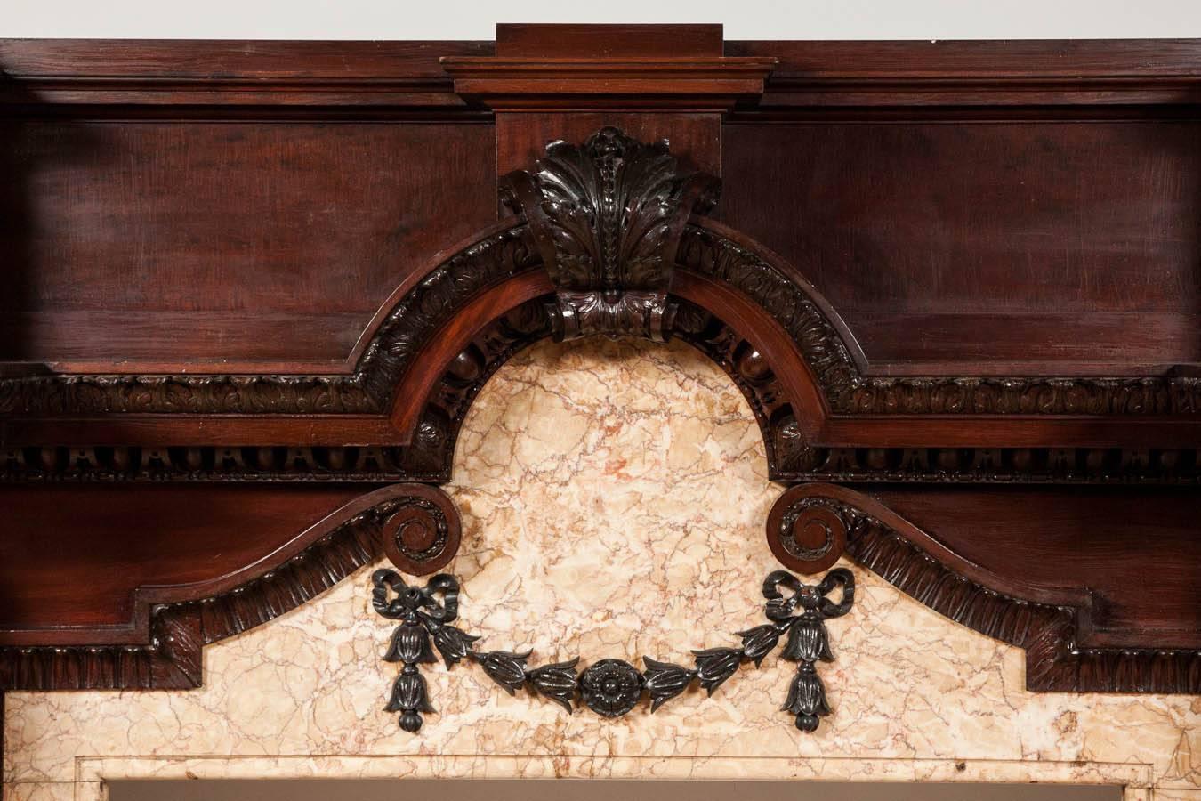 A pair of magnificent Baroque style fire surrounds in carved mahogany, with marble slips. These ornate and elaborate fireplace surrounds feature masked corbels with bell flower pendants on the front and side of both jambs, a central radius top to