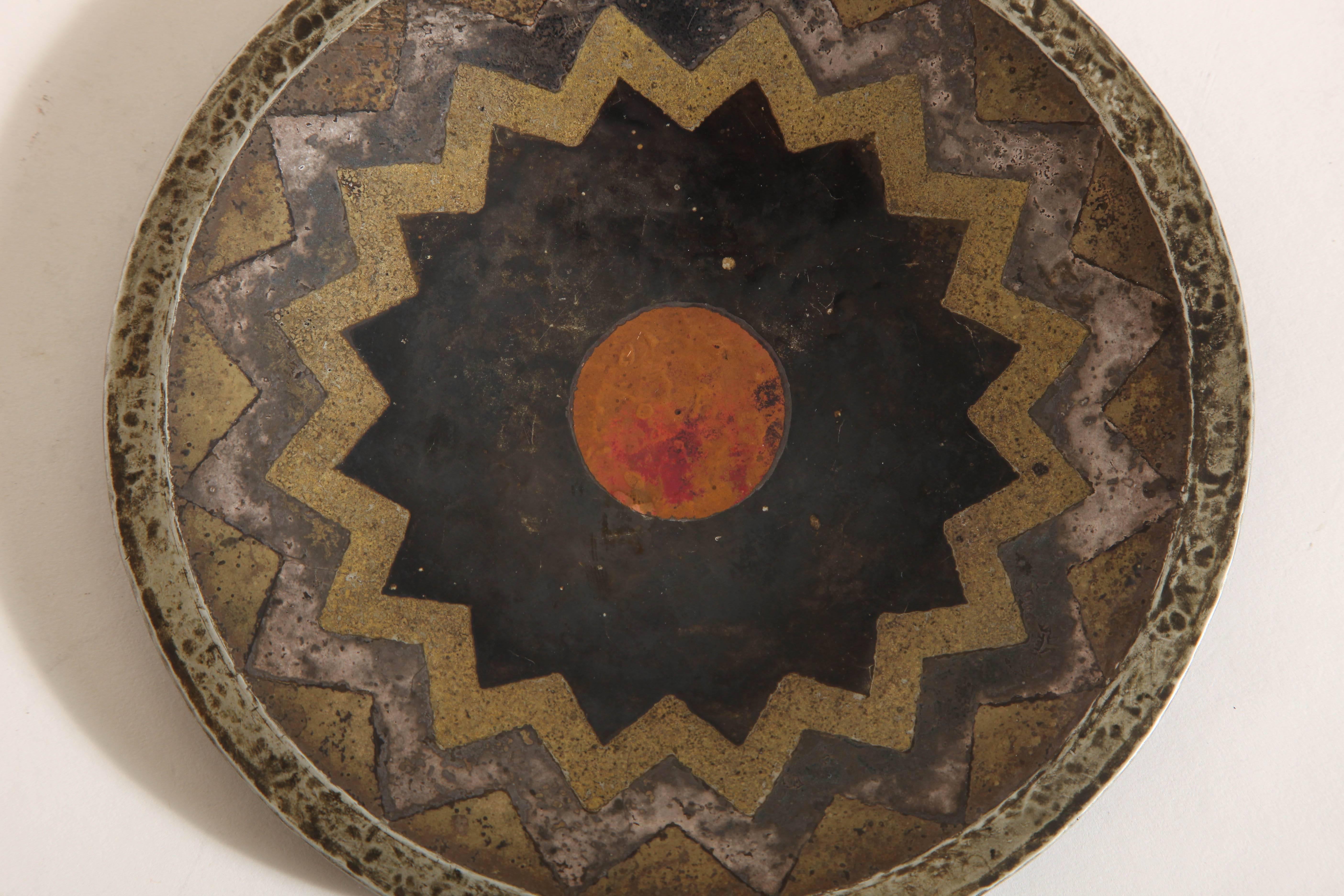 Copper dinanderie coupe with gilded patina and silver, gold and black geometric design and central red copper circle.
Inscribed CL LINOSSIER/ A SON AMI PH. BURNOT EN GAGE D’AMITIE 1926 underneath.

Provenance:
Philippe Burnot
Collection