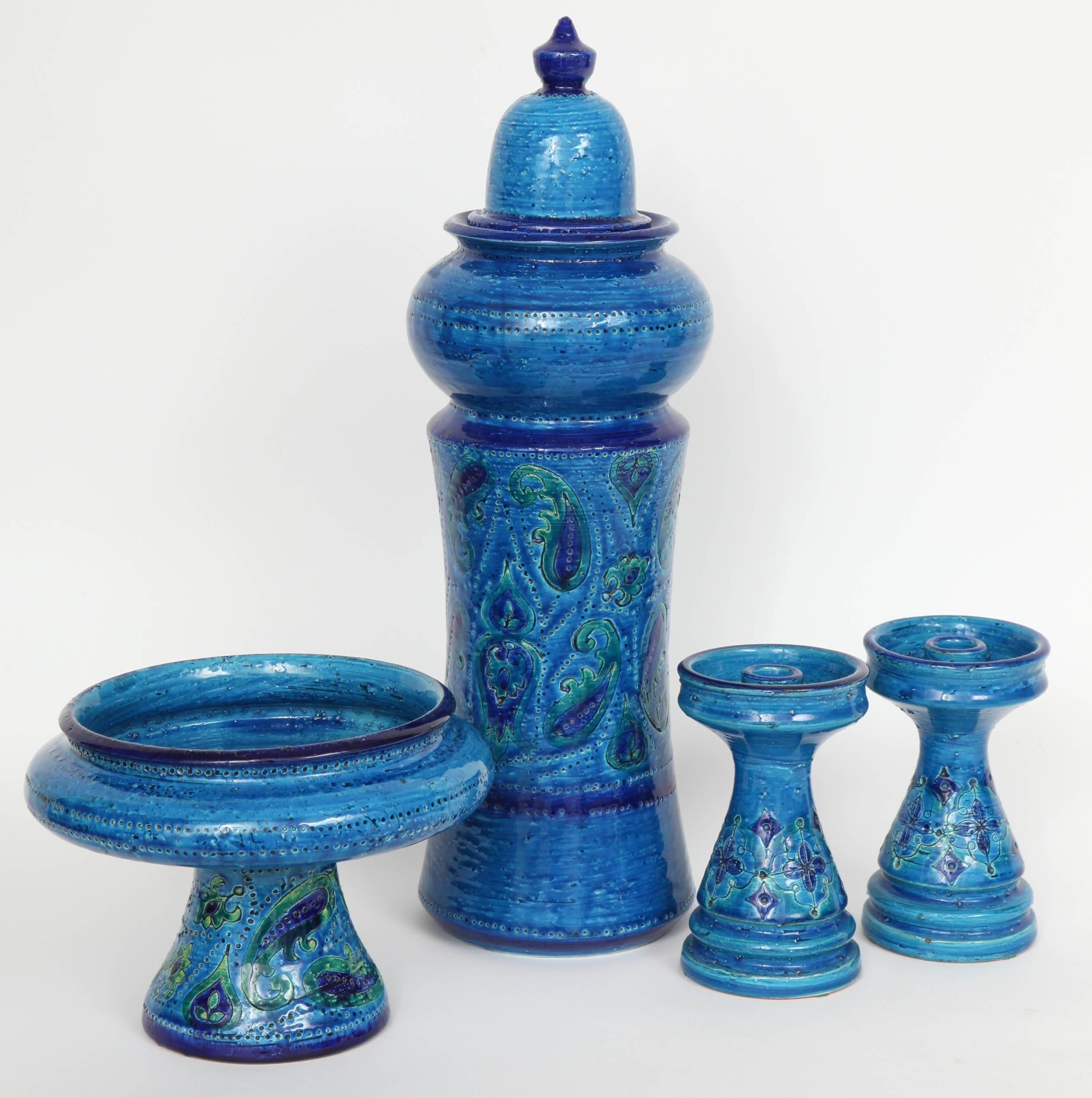 Four-piece Rimini blue glazed ceramic set composed of a compote, cannister and a pair of candlesticks. Pieces feature the iconic blue glaze with incised details. Pieces marked Italy on bottom.

Compote measures 9