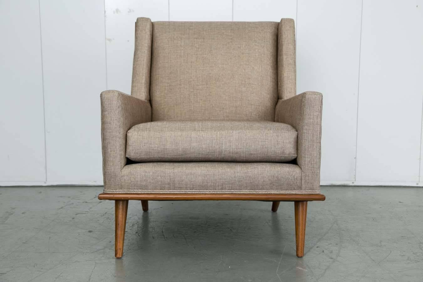 A nicely angled Mid-Century lounge or club chair newly upholstered in a metallic taupe linen with original finish exposed mahogany trim over tapered legs.