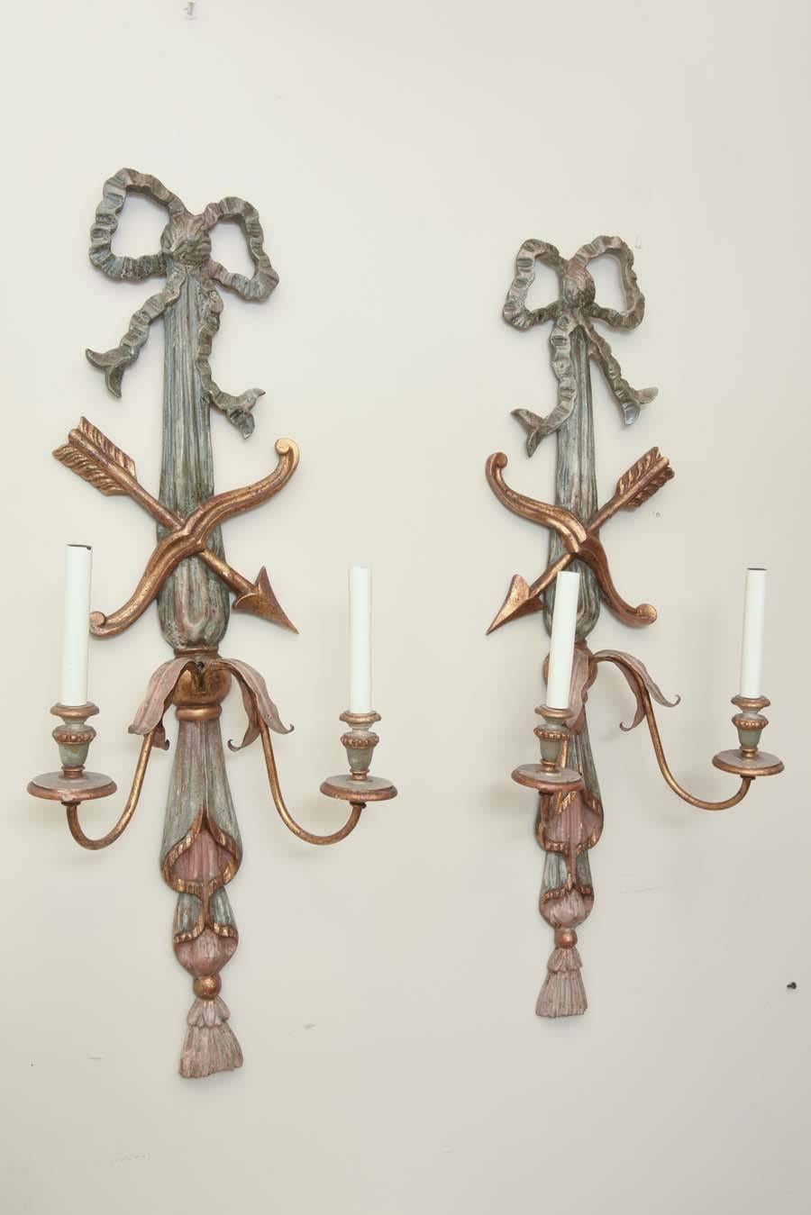 Opposing pair of carved wood sconces, painted and parcel gilt, each shaped as draped fabric surmounted by a bow, having crossed arrows, two scrolling iron candlearms with wood candlepots. Electrified.

Stock ID: D4962