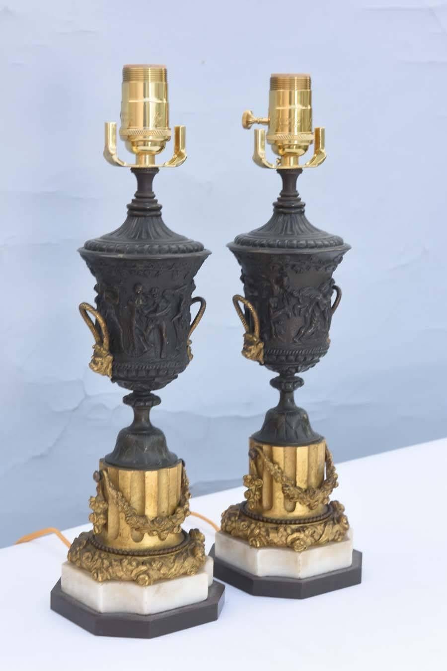 Paire de lampes finement ciselées, chacune ayant une urne campane couverte, en bronze patiné, avec des poignées dorées, sur un pied rond, reposant sur un socle à colonnes cannelées et festonnées, et une base en marbre graduée.

Stock ID : D8630