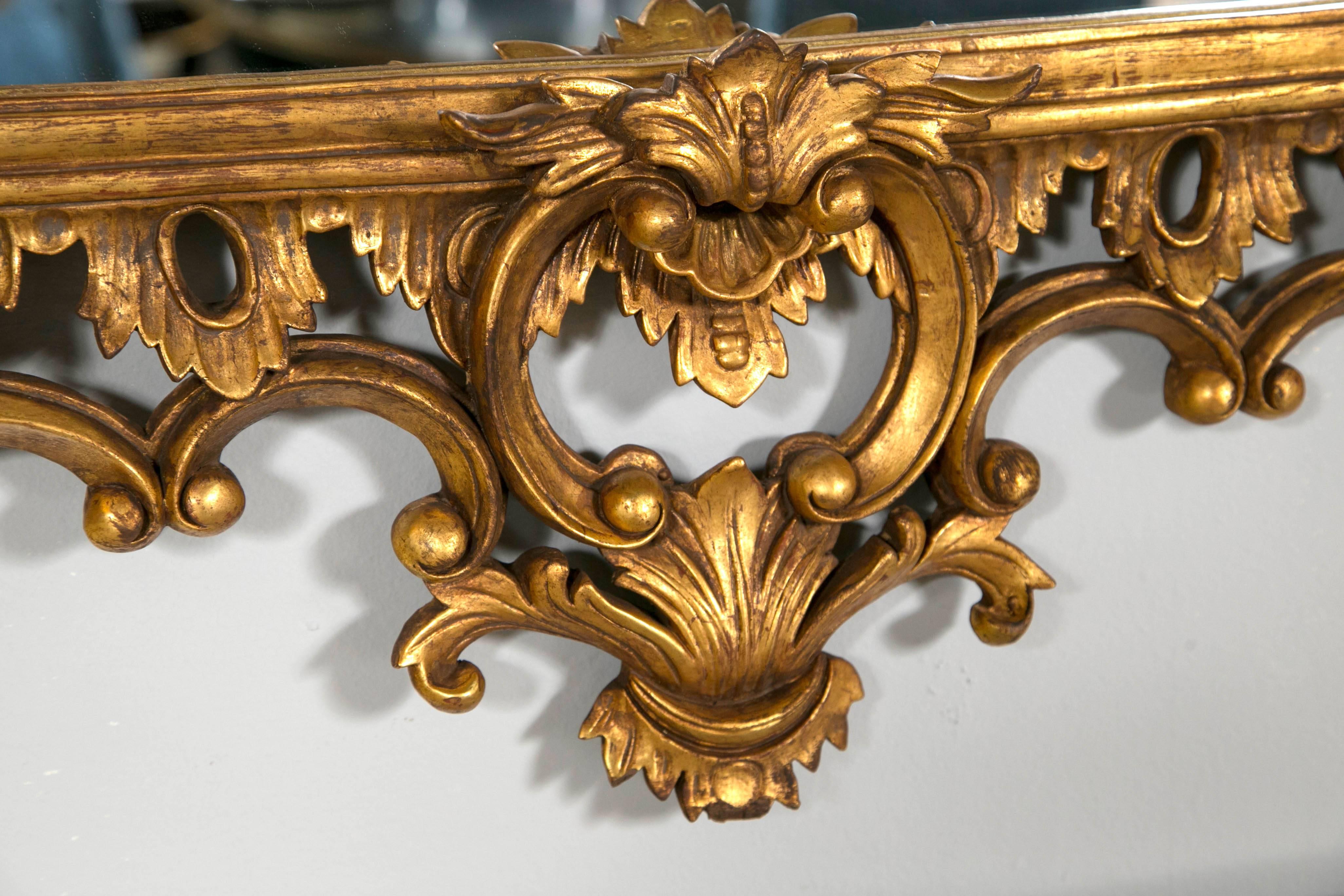Pair of Chippendale giltwood carved wall or console mirrors. Each clean and clear center mirror framed in a spectacular carved gilt wooden frame with leaf and vine with scroll design. The backs all wooden. The open fretwork design on this fine pair