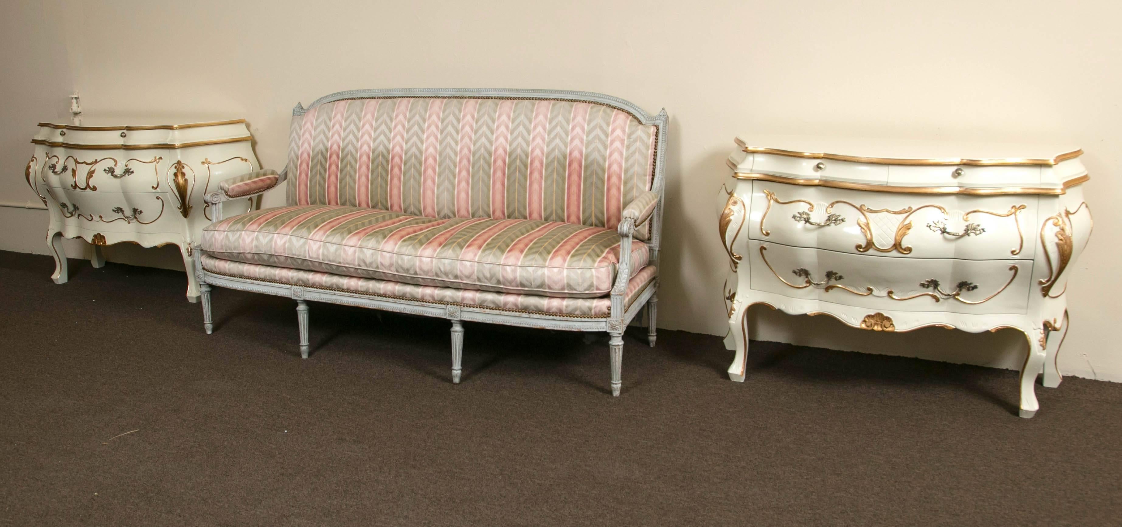 Pair Parcel Paint and Gilt Decorated Bombe Commodes. This stunning pair of Hollywood Regency style pair of commodes are finely painted in an off white finish with fine clay under gilt hi lights. Each having two small drawers above two large drawers.