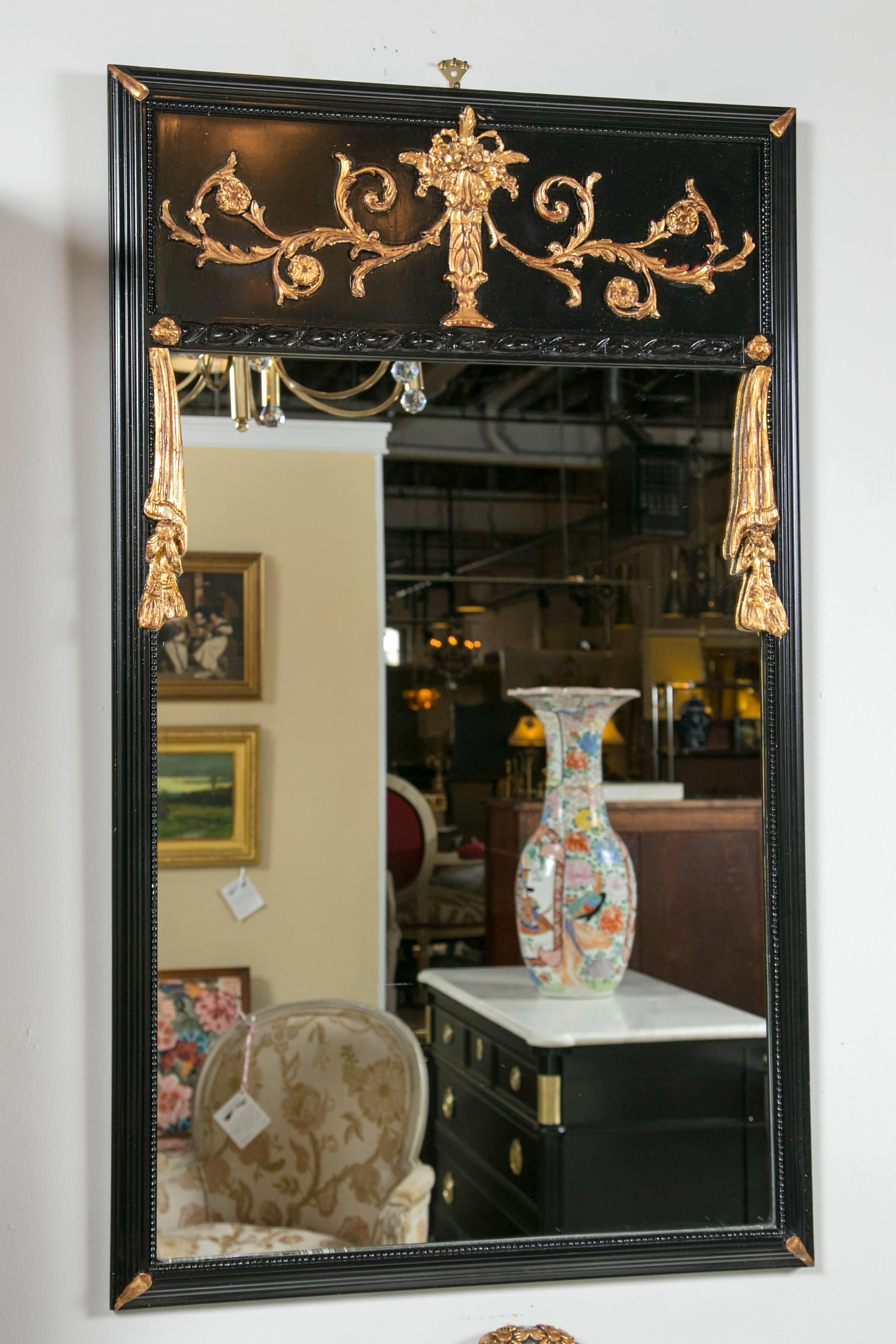 Pair of Ebonized Gilt Drapery Form Carved Trumeau Mirrors.  Each ebonized frame having gilt leaf corners flanking a clear clean mirror. The ebonized top panel having a gilt gold solid wooden carved basket with flowing leaf and vine design. The sides