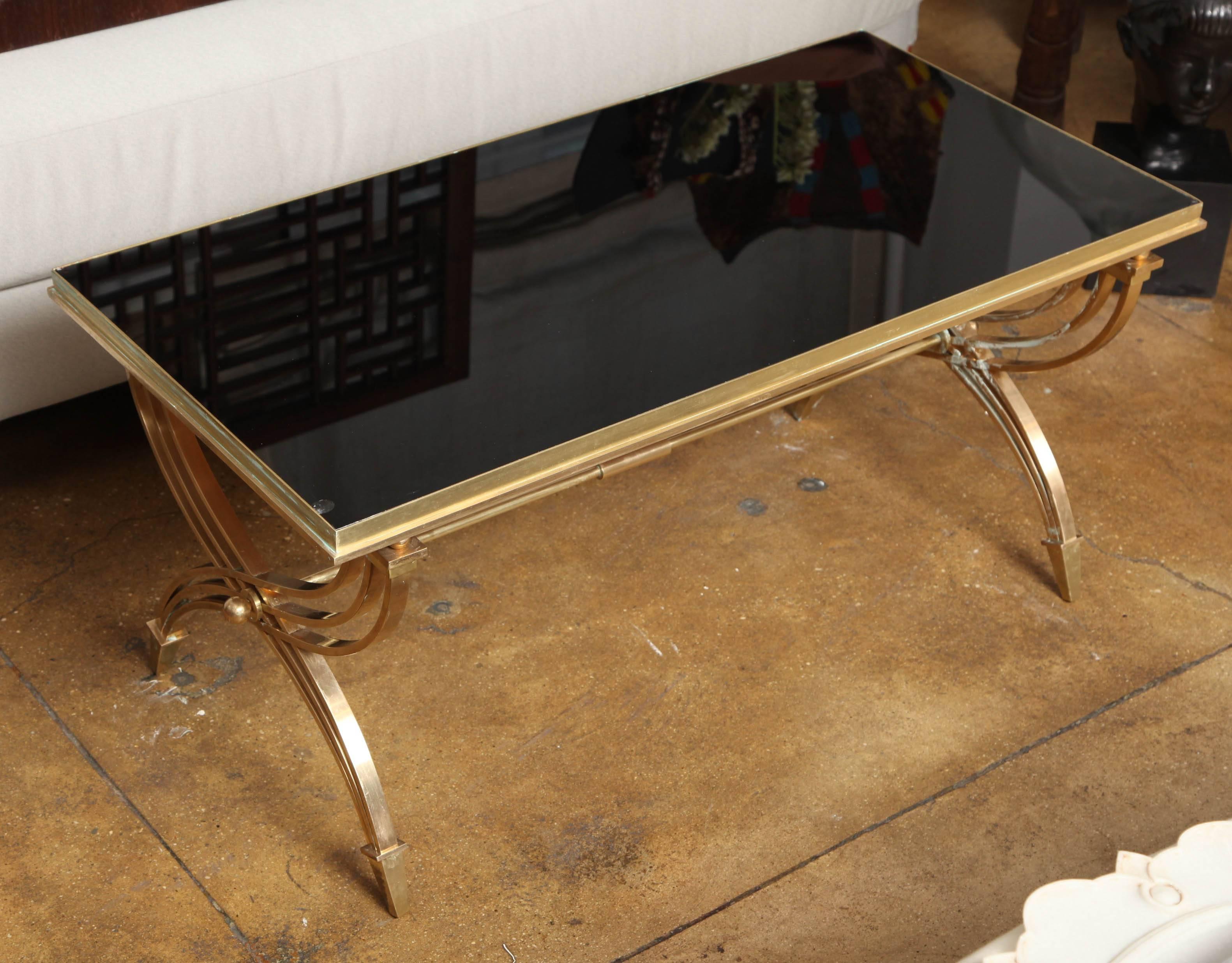 A coffee table with black back-painted glass on a wrought brass frame and base, from France.
