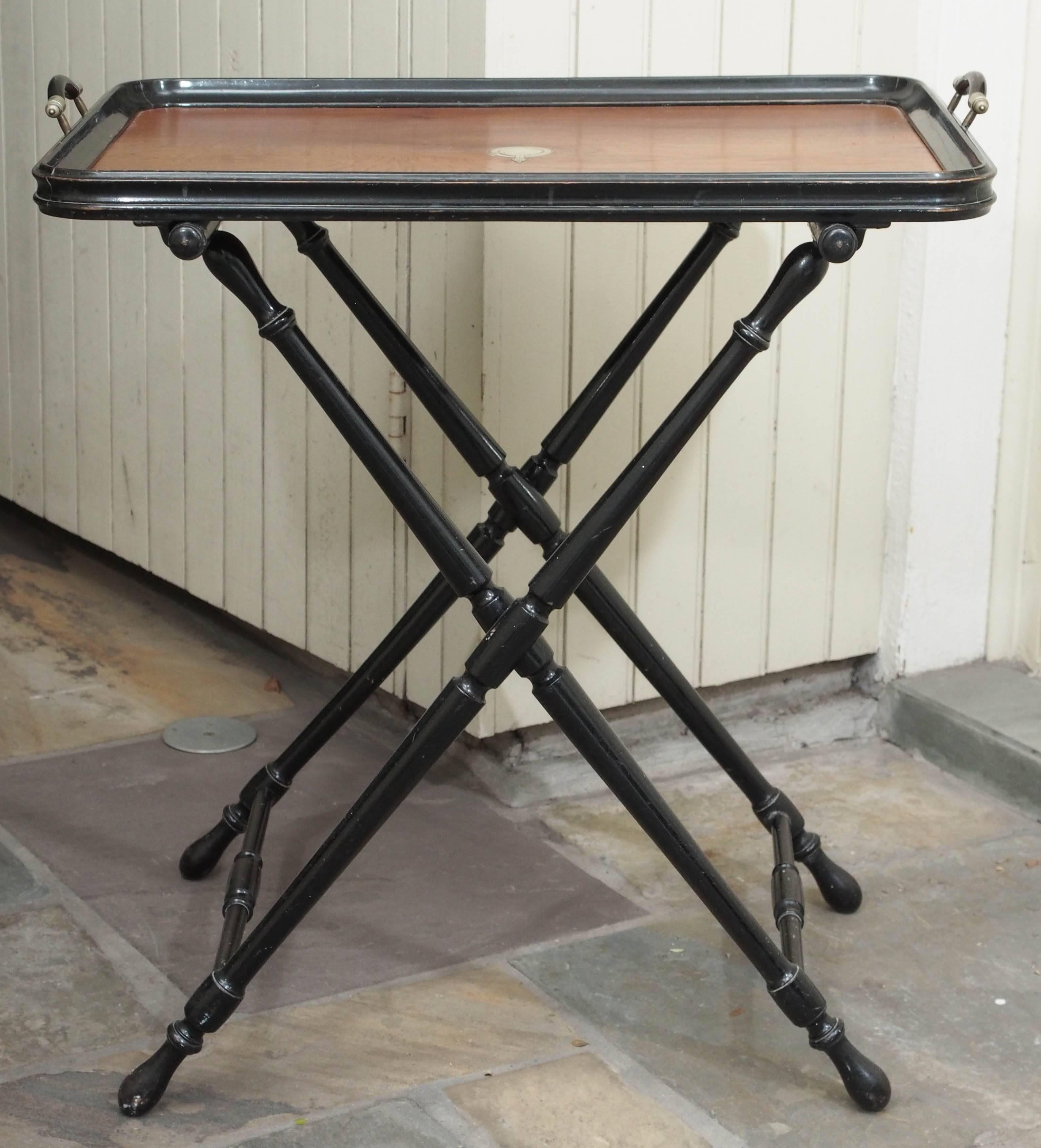 Butler's tray, French, circa 1900. Wood with ebonized trim. Tray is 19 inches by 27 inches with brass medallion in center, set on turned, ebonized trestle legs. Will fold for storage.