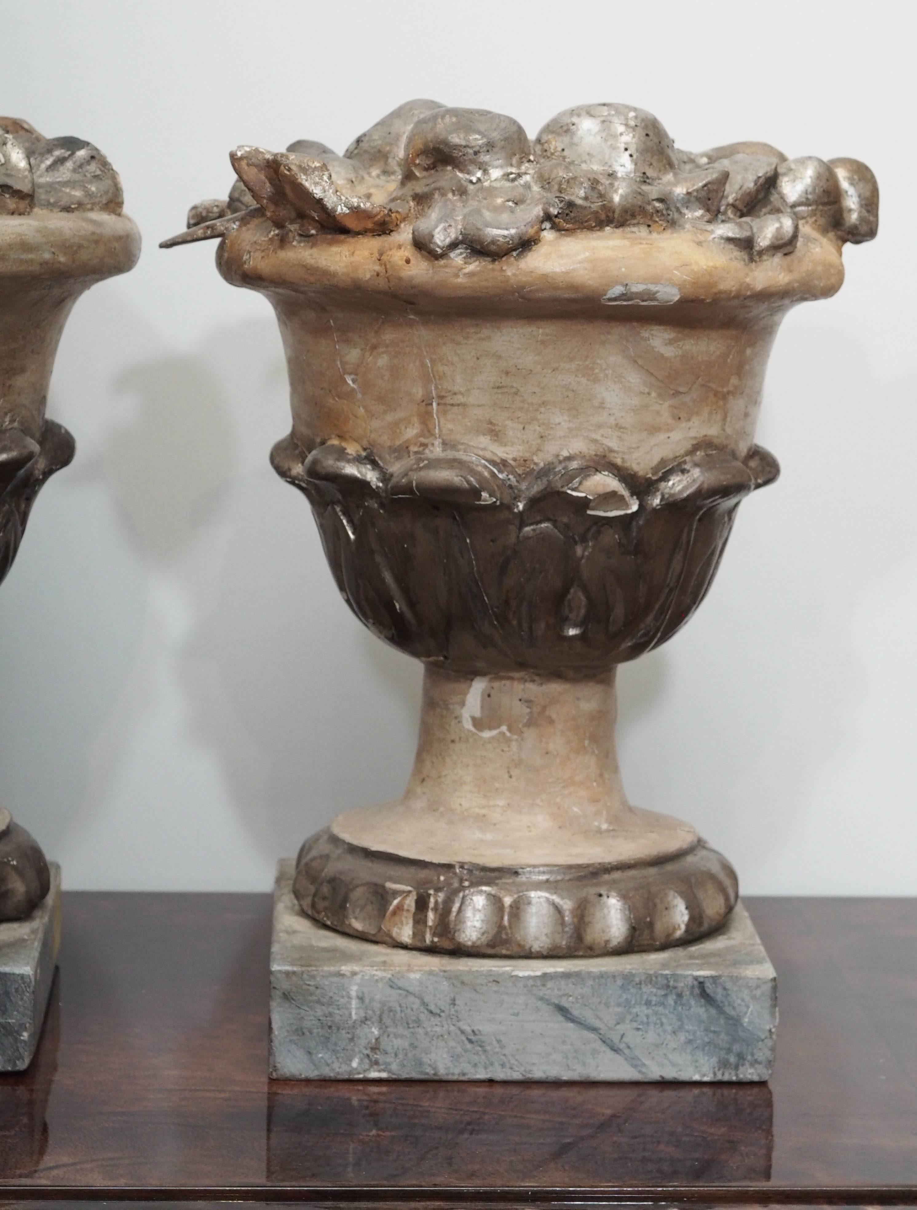Two carved and silvered Bacchanalian wooden bowls of fruit on wooden pedestals.