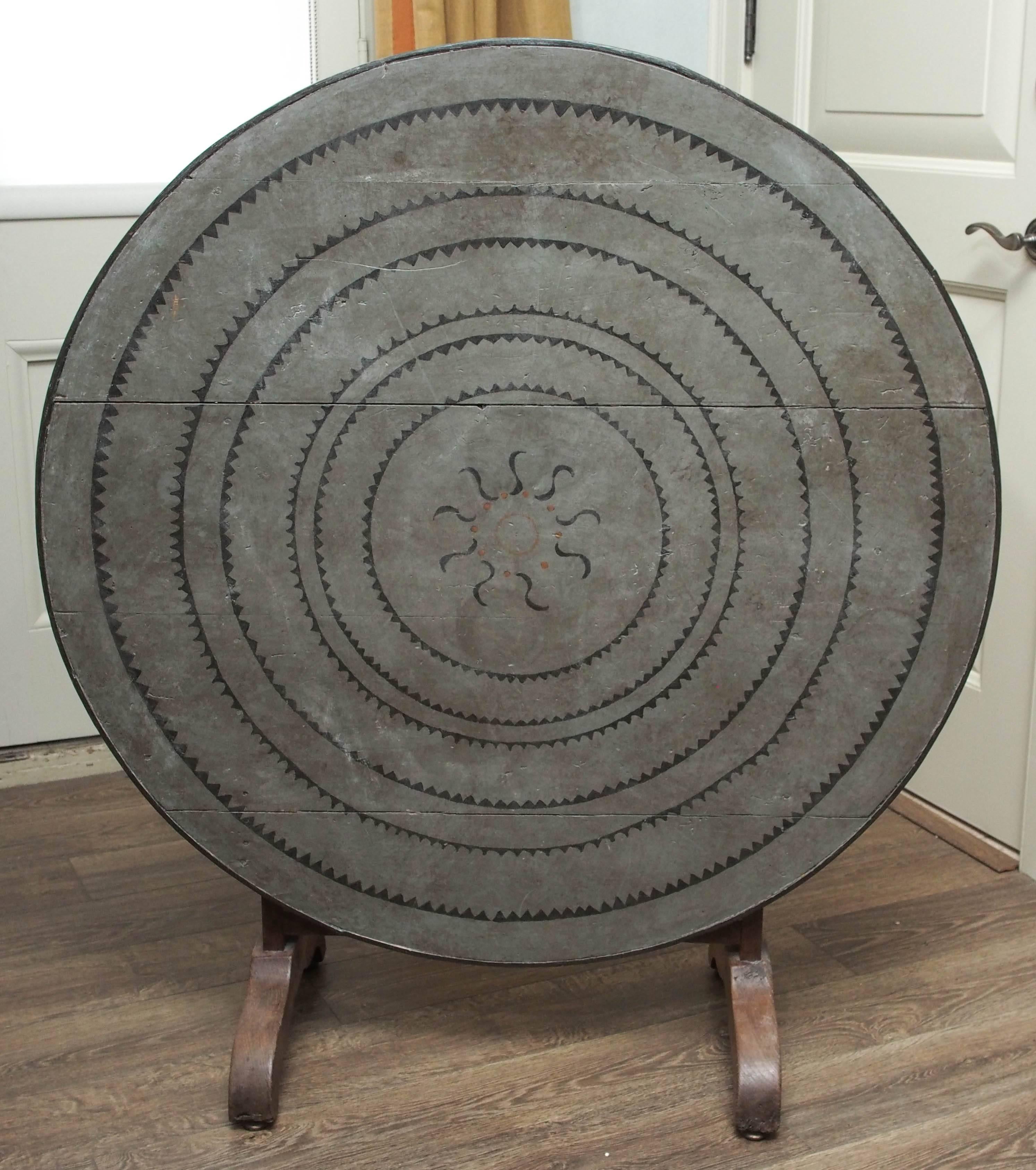A beautiful turn of the century French oak wine table with a painted canvas cover. The cover features a graphic of a sun centered inside radiating rings of light. The occasional table also folds for storage.