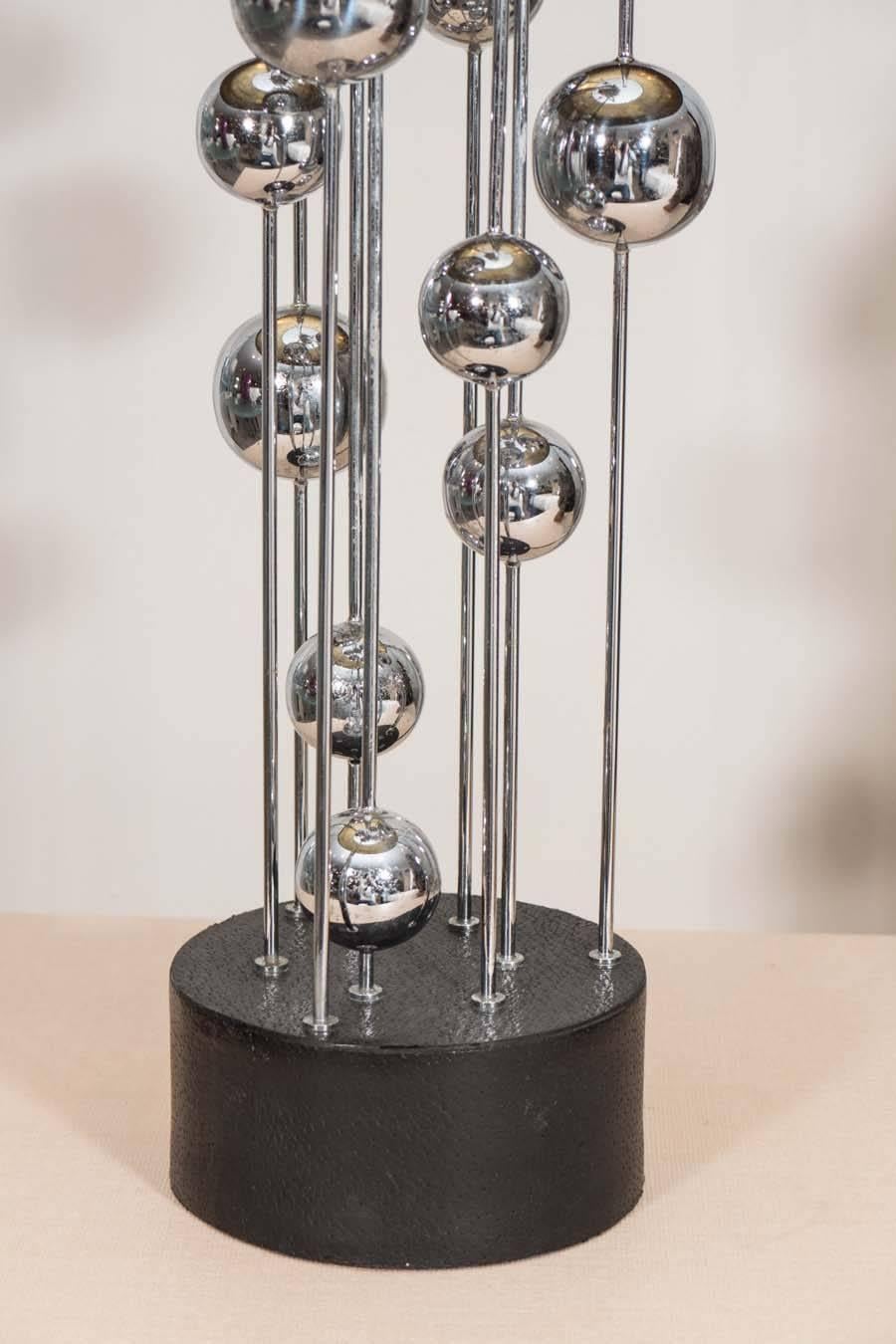 Assorted chrome spheres on metal rods affixed to a round Lucite disc on to and a thick black painted wood base. (Shade not included).