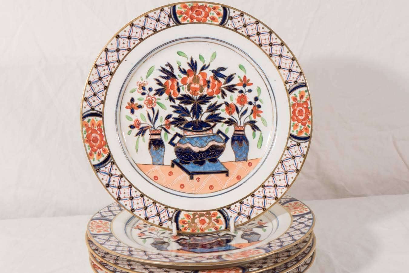 A set of 14 English dishes with a traditional Imari design showing three flower filled vases on a garden terrace. The addition of green in the leaves energizes the scene. The border is patterned with diamonds and four panels with flowers.
 