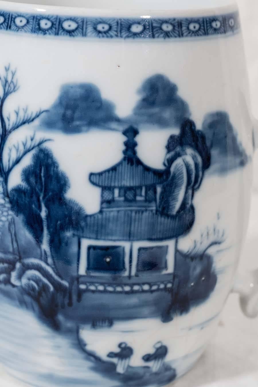 A large Blue and White Chinese porcelain mug hand-painted with a continuous scene showing a pagoda set amid exotic trees and mountains. The large cylindrical body has a loop handle with molded thumb and finger rests in the shape of ruyi* (see images