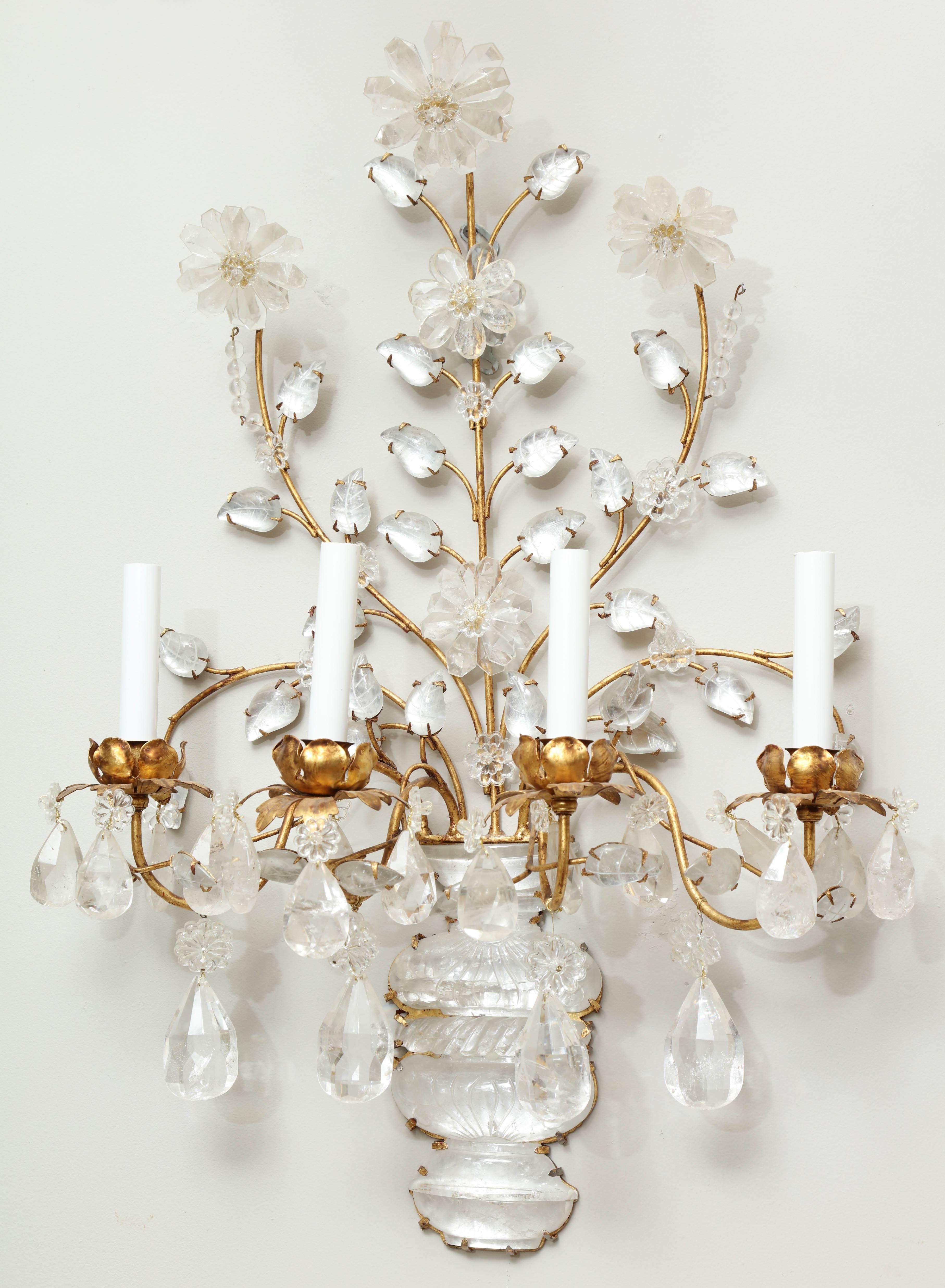 A pair of four light gilt iron wall sconces with molded and carved rock crystal vase shaped backplates, issuing branch form candle arms with flower shaped bobeches, the frames draped with rock crystal drops.