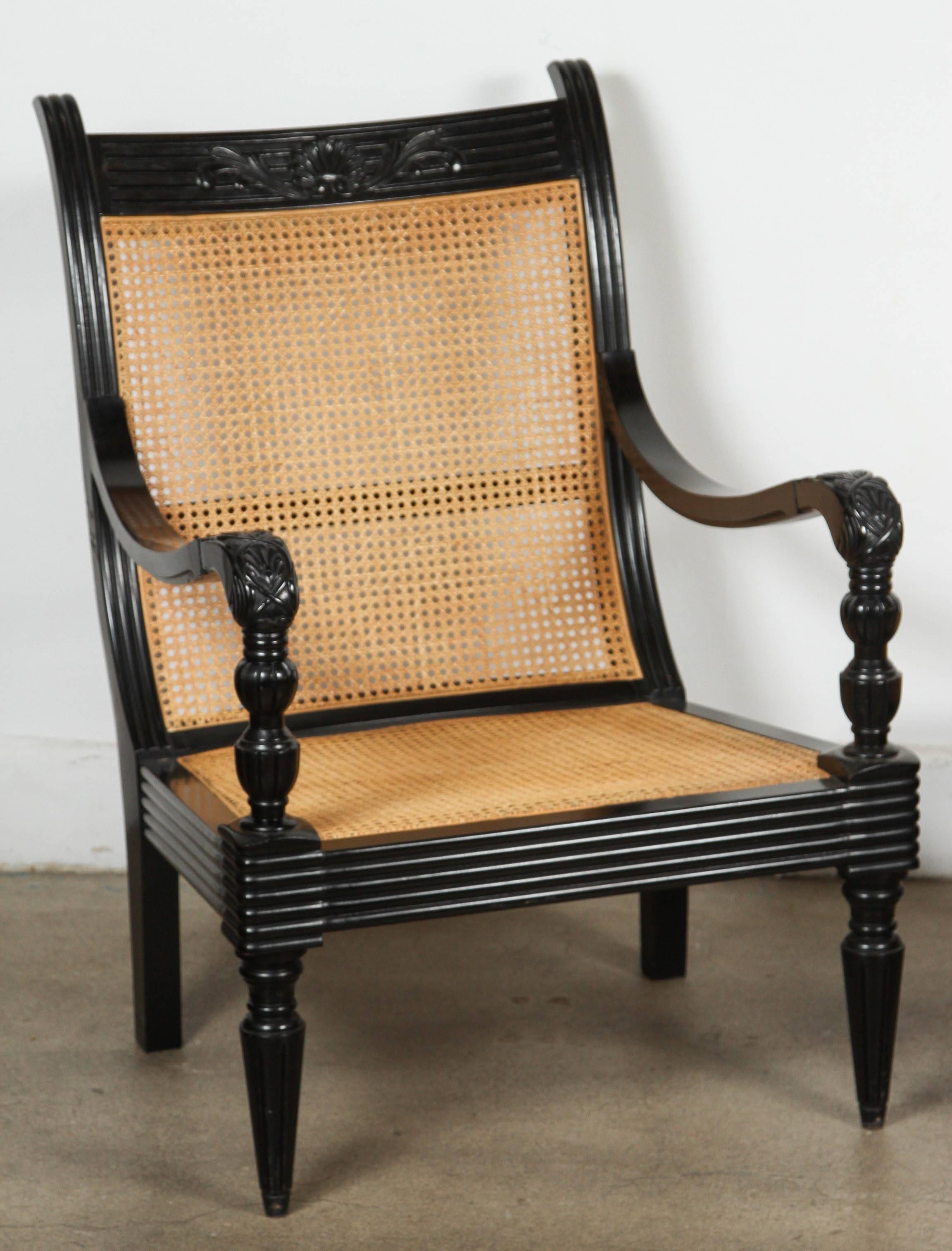 Beautifully carved ebonized black lacquered Anglo-Indian armchair with cane and ottoman or side table.
Carved foliage on the backrest and arms.
Cane is in excellent condition. 
Ottoman size is: 26" x 26" x 26".