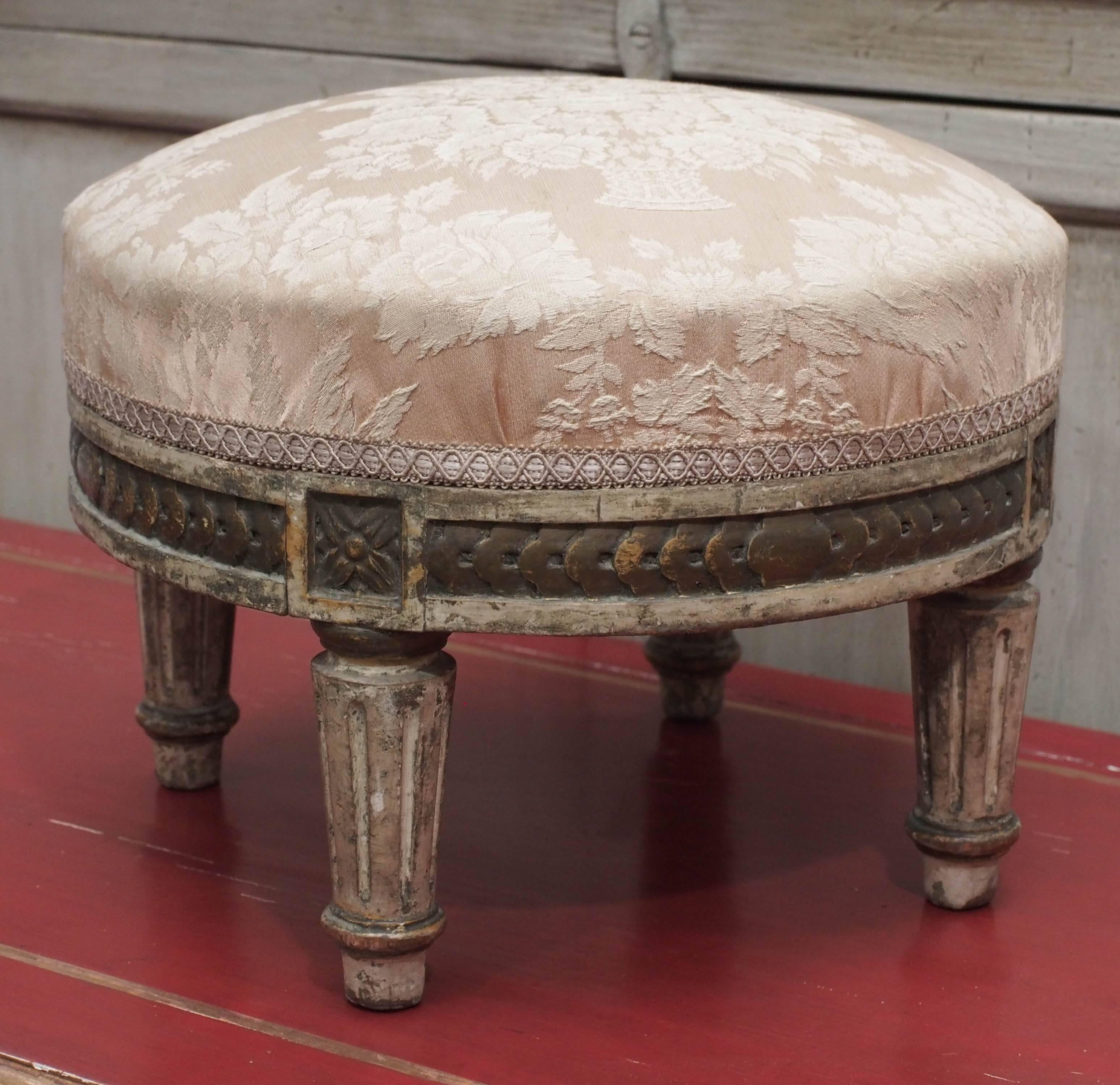 Pair of petite French Louis XVI style footstools or ottomans. Carved and upholstered. Some traces of original paint. Most likely dating to the early 19th century.