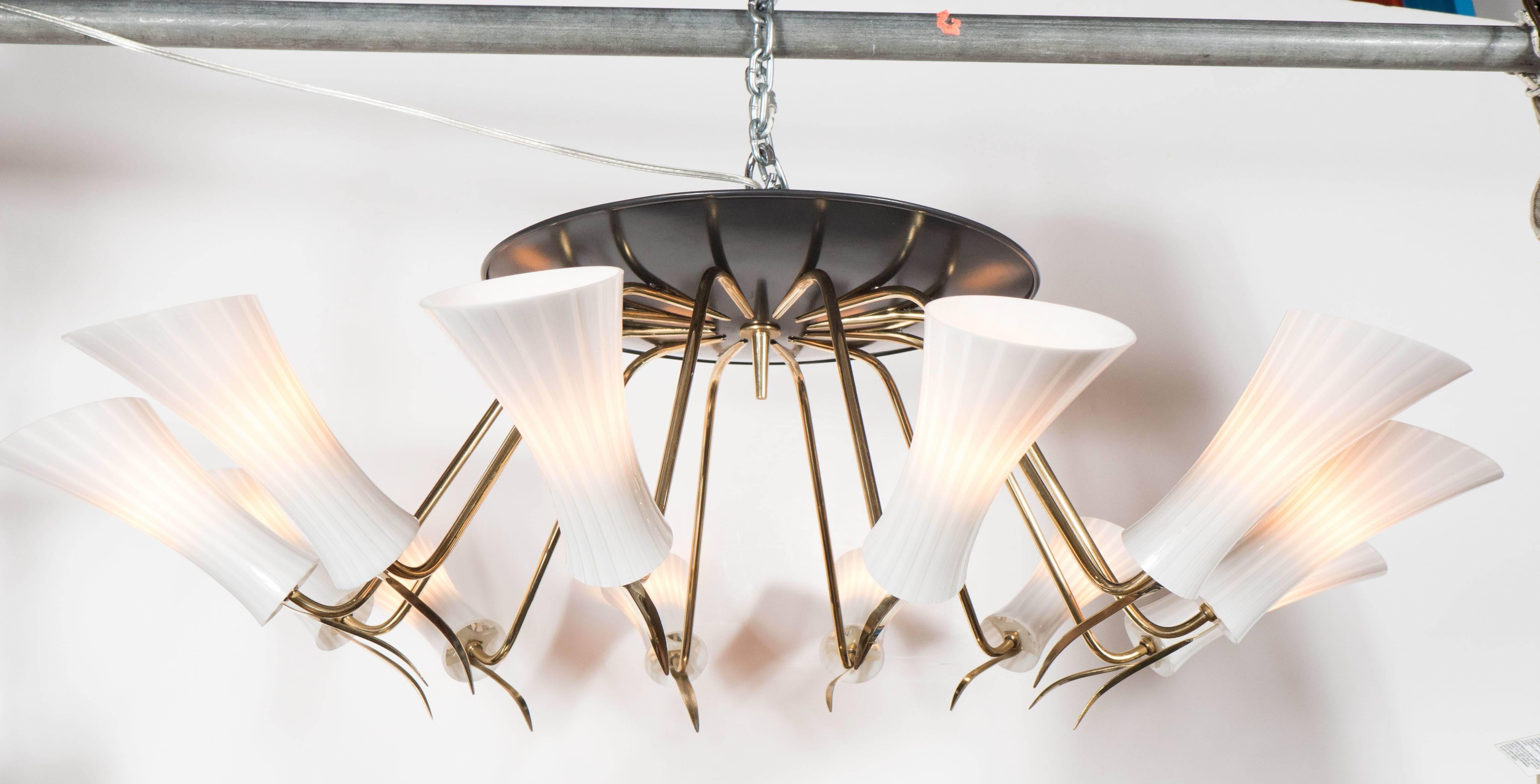 A beautiful Mid-Century Modernist chandelier in the manner of Stilnovo featuring a black enameled base which supports twelve extension arms of polished brass arms each supporting a handblown Murano glass shade with linear striations. The detailing